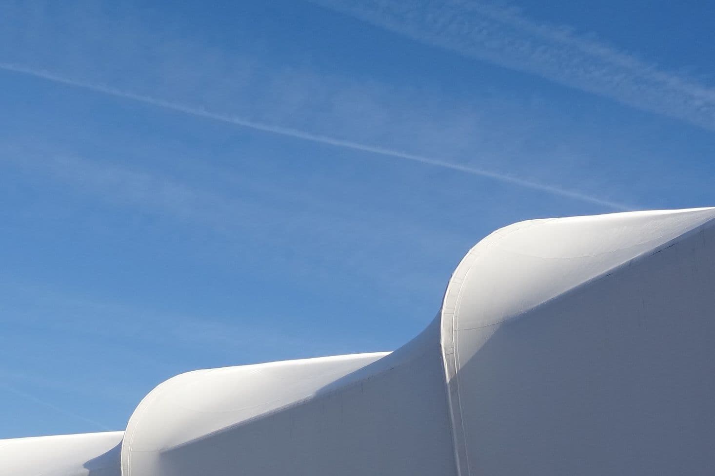Eine weiße, segelartige Konstruktion ist vor blauem Himmel zu sehen
