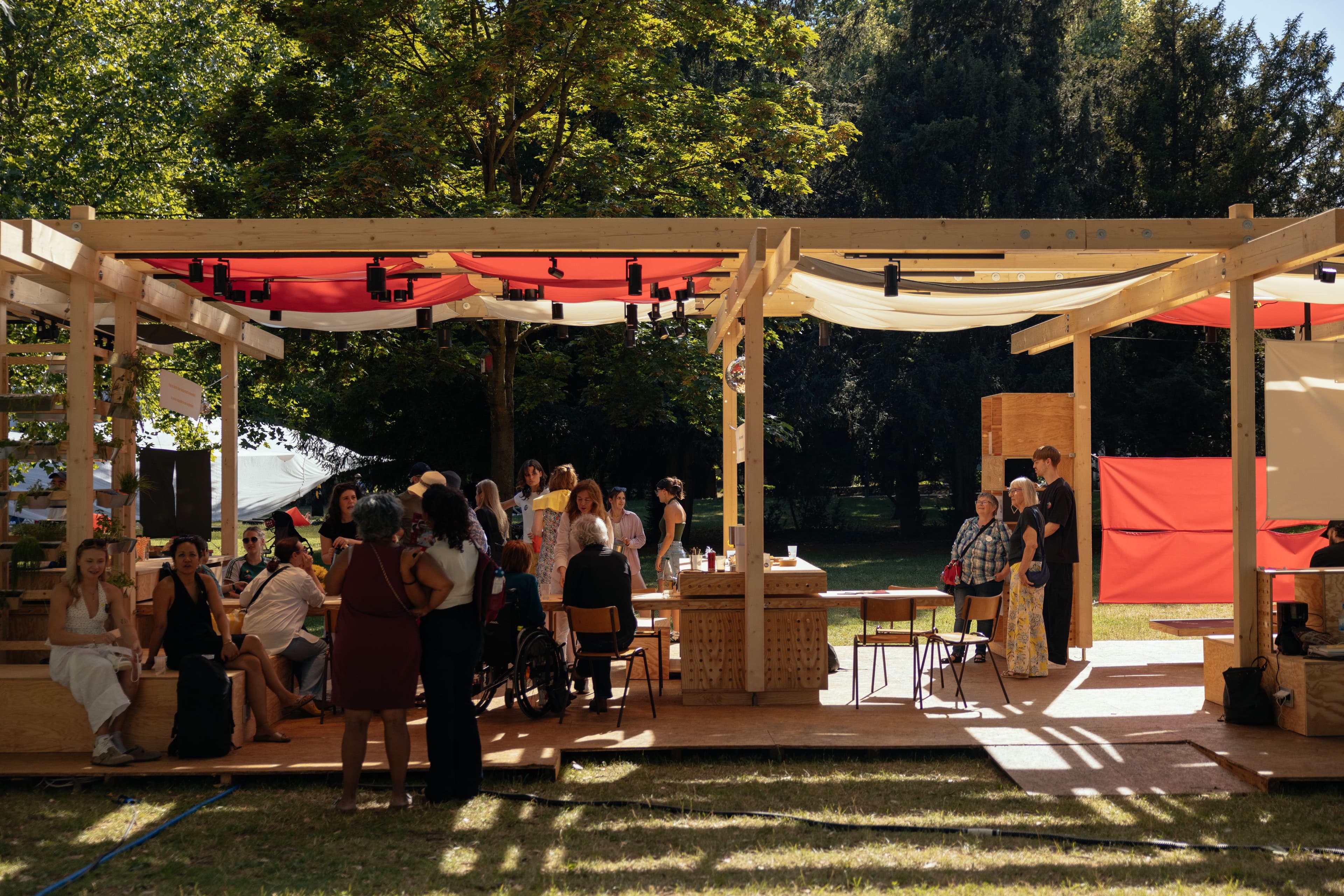 Mehrere Personen stehen unter einem Holzpavillon im Grünen.