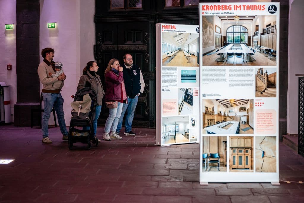 Menschen stehen in einer Ausstellung und schauen sich Infos und Bilder an.