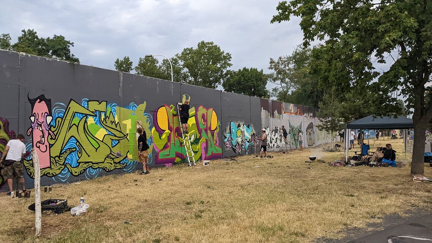 Verschiedene Personen besprühen eine Graffitiwand.