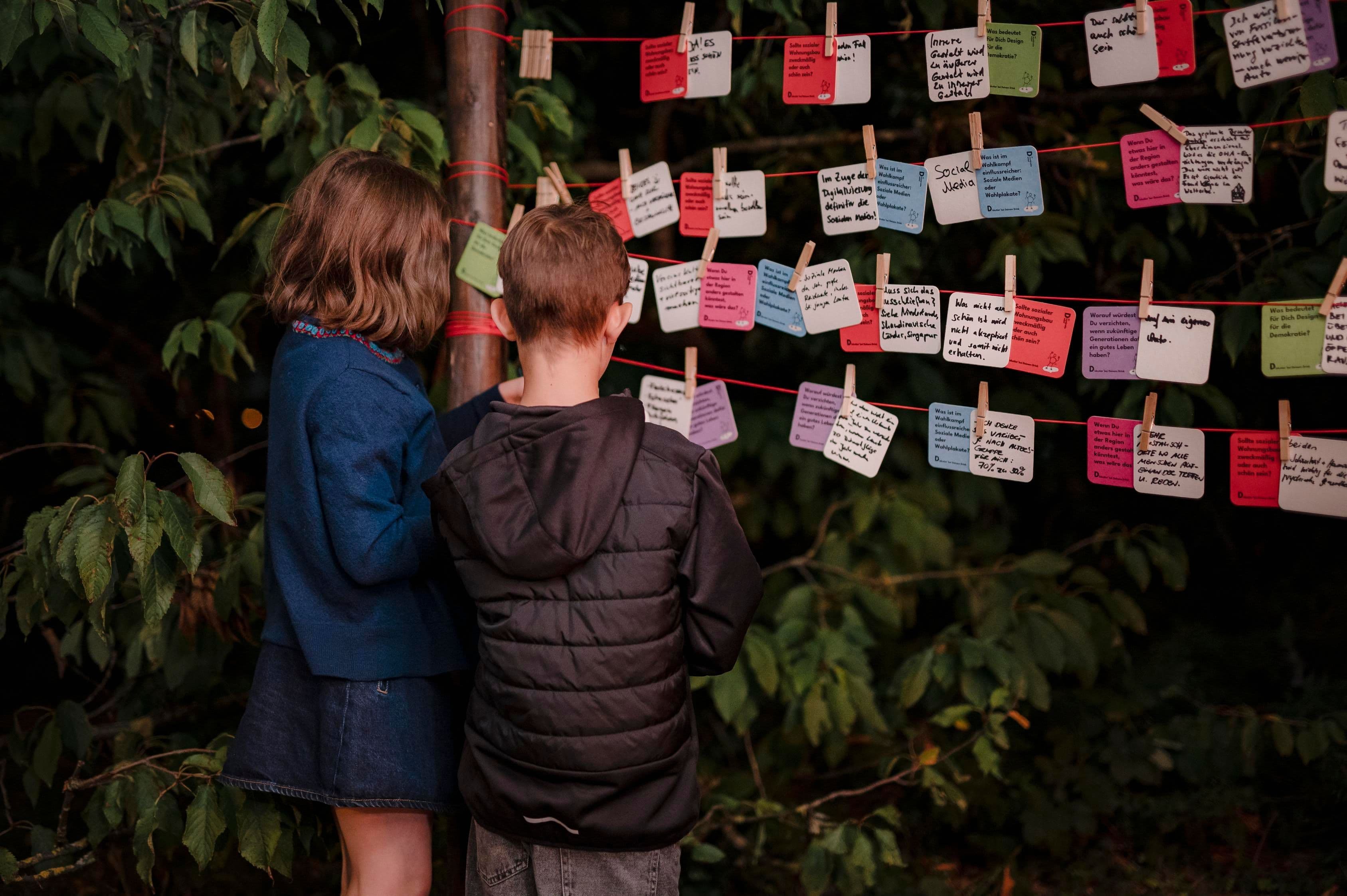 Kinder stehen vor mehreren beschrifteten Bierdeckeln.