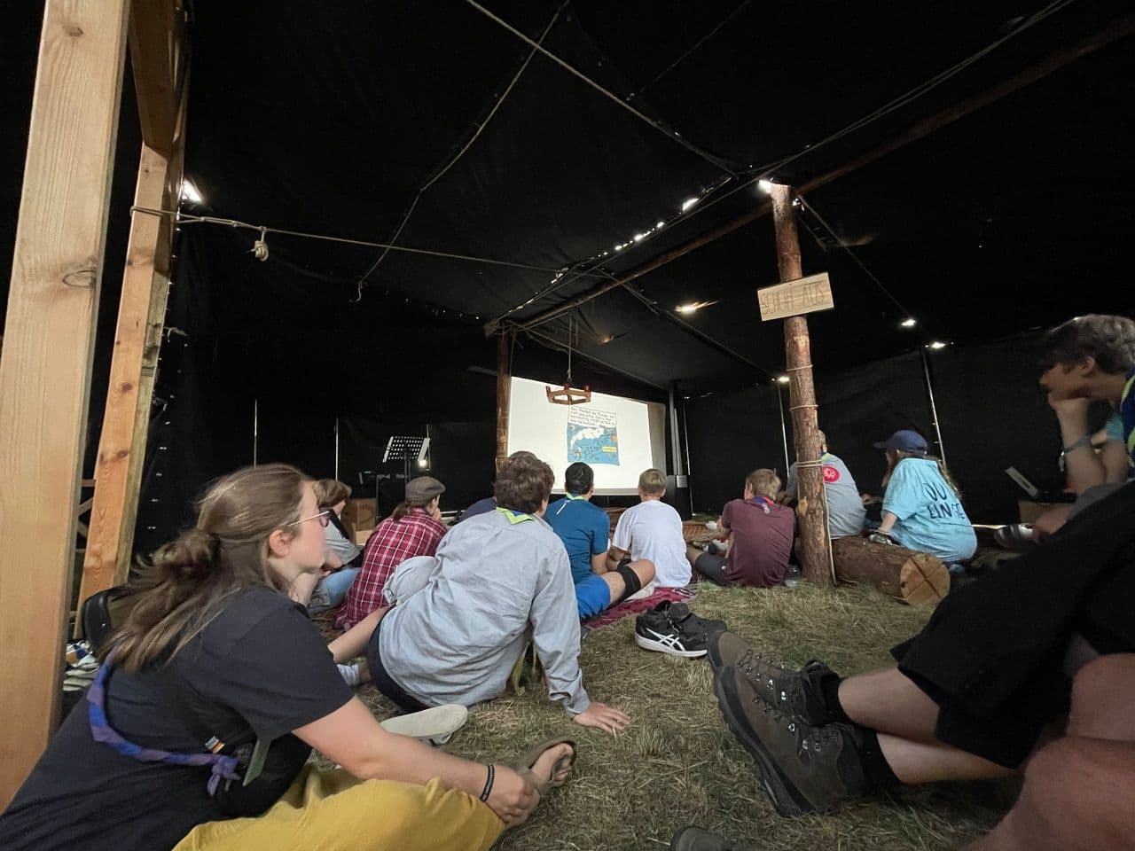 Menschen sitzen vor einer Leinwand am Boden mit Heu
