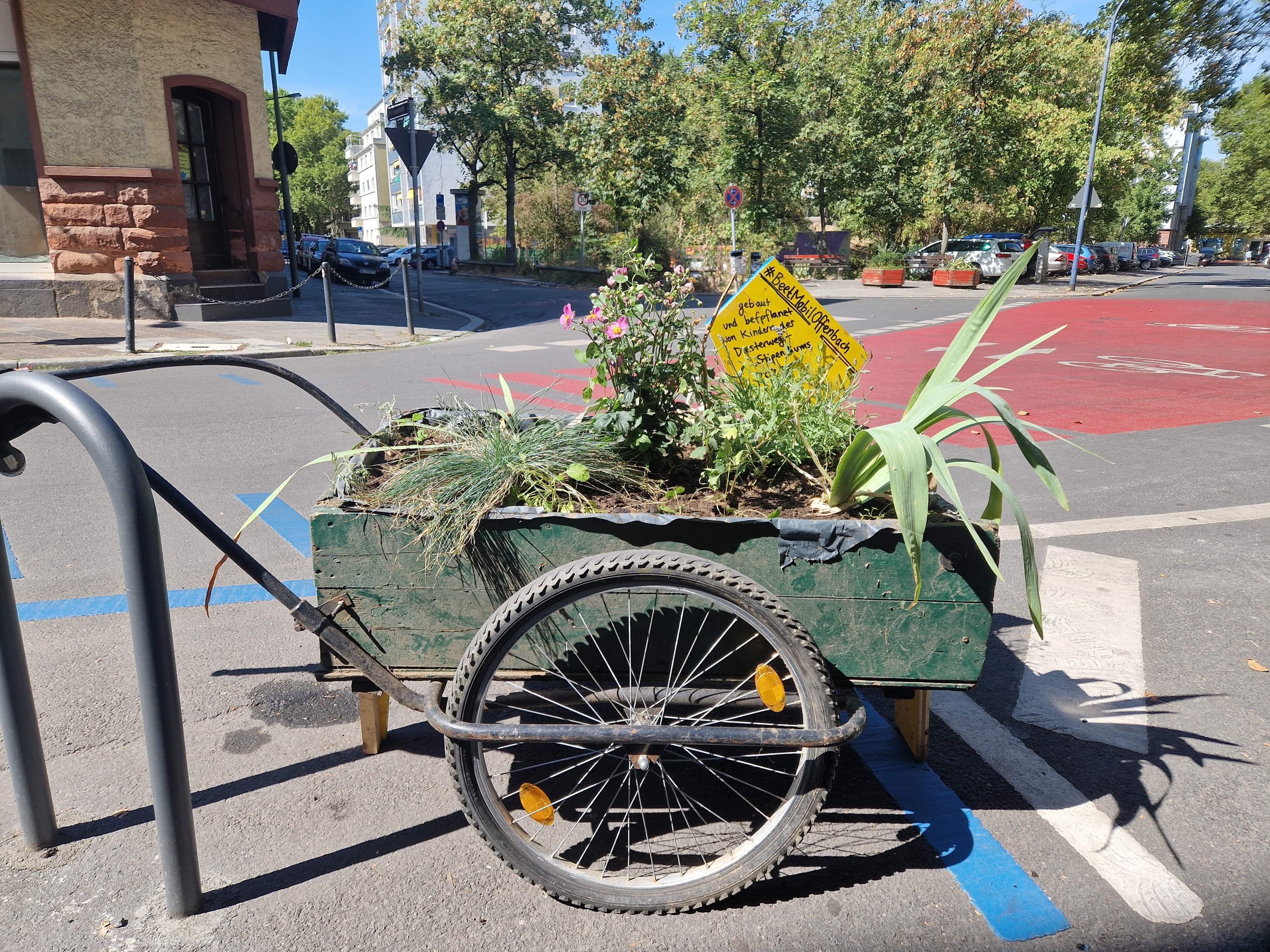 Ein kleiner Anhänger, gefüllt mit Erde und Pflanzen, steht auf der Straße.