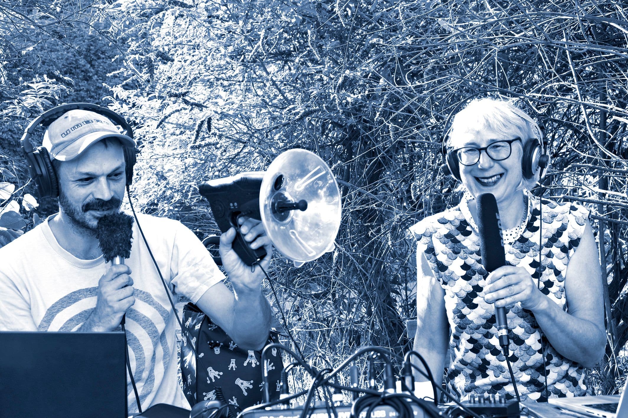Ein Mann und eine Frau hantieren mit Mikorfonen und einem Aufnahmegerät und lachen dabei