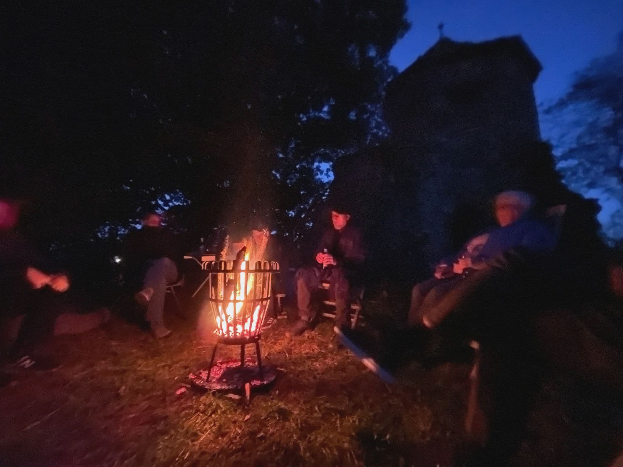 Menschen sitzen vor einem Lagerfeuer in der Abenddämmerung