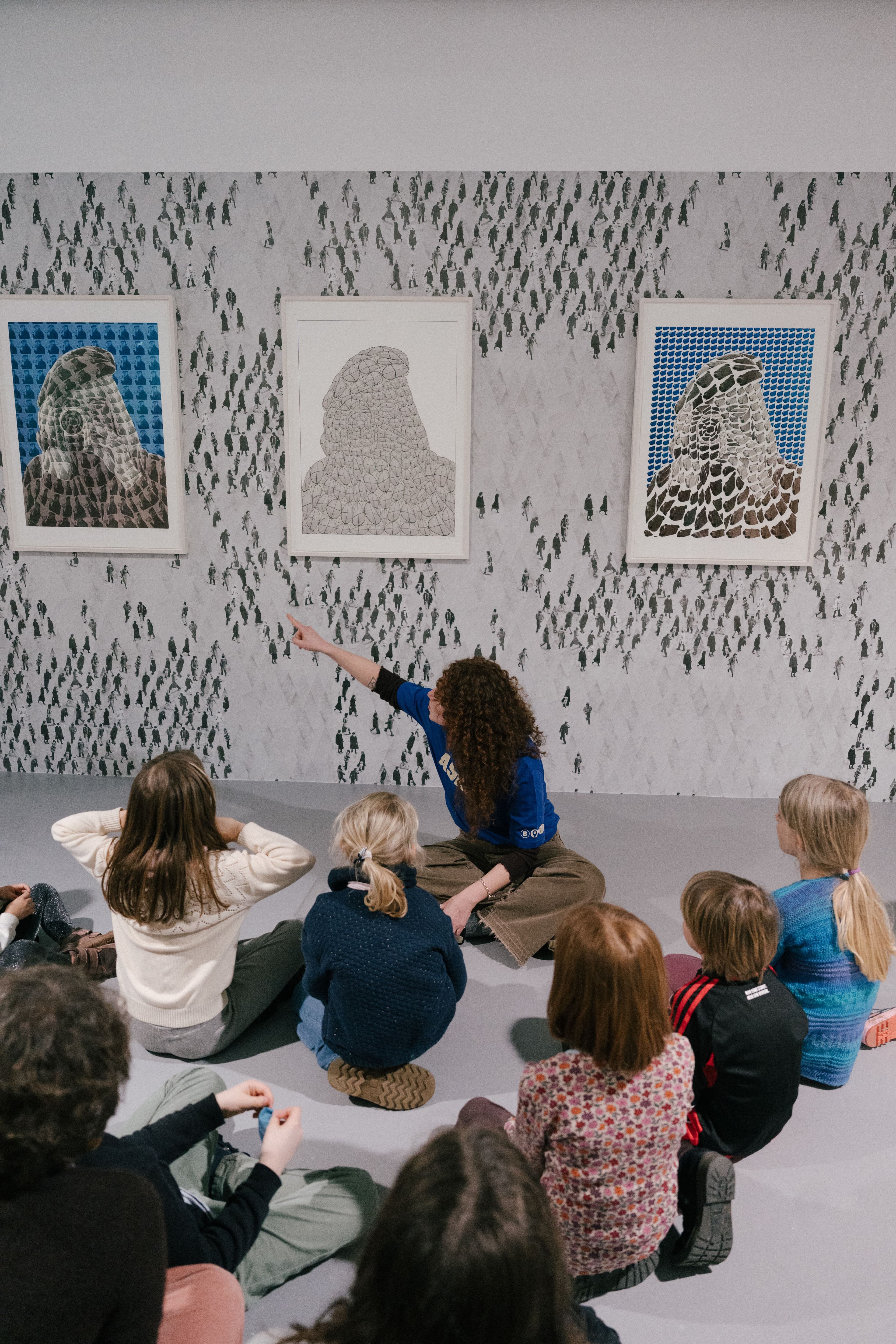 Mehrere Kinder sitzen im Museum auf dem Boden vor Bildern an der Wand.