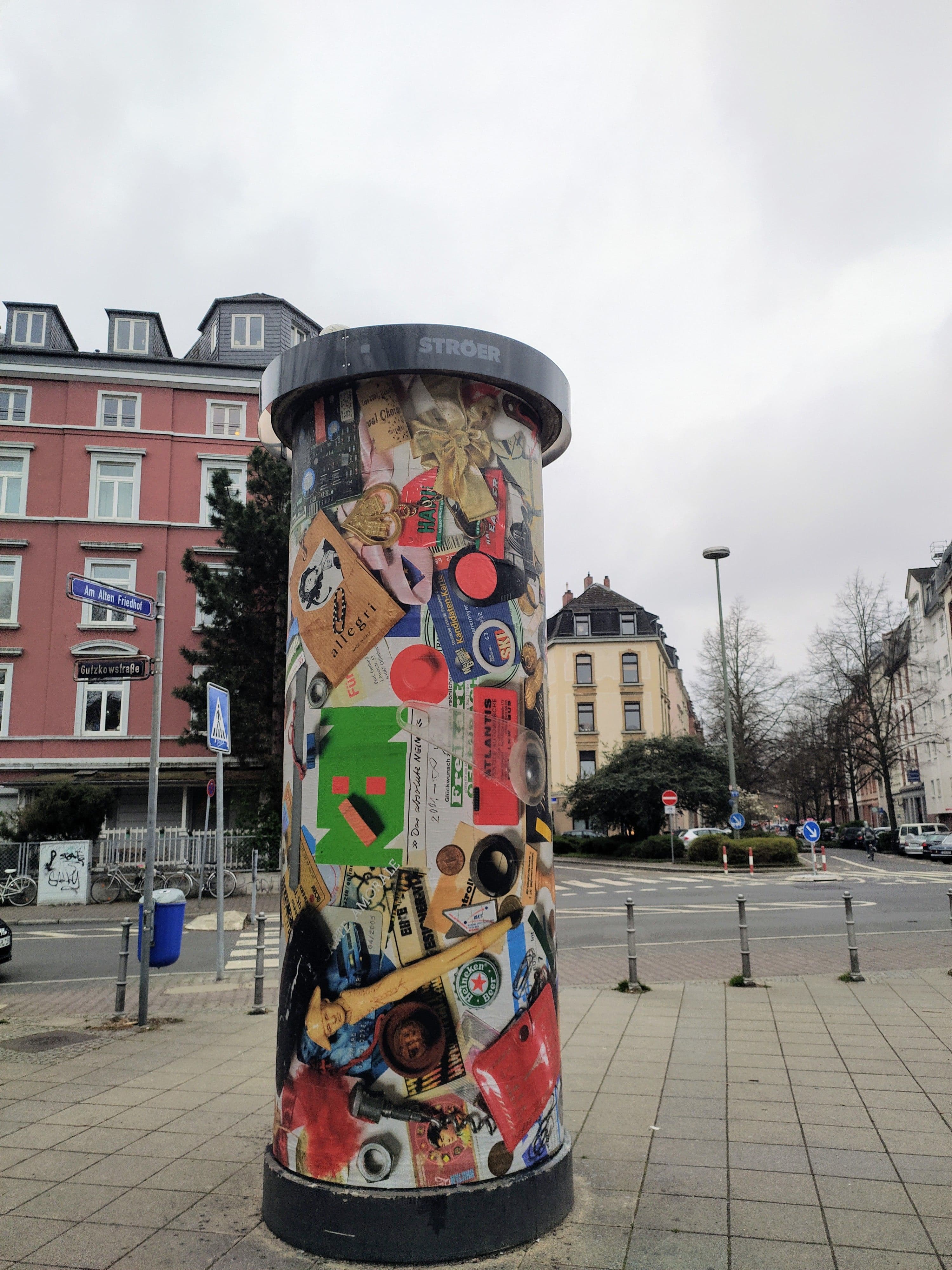 Eine bunte Litfaßsäule steht an einer Straße.
