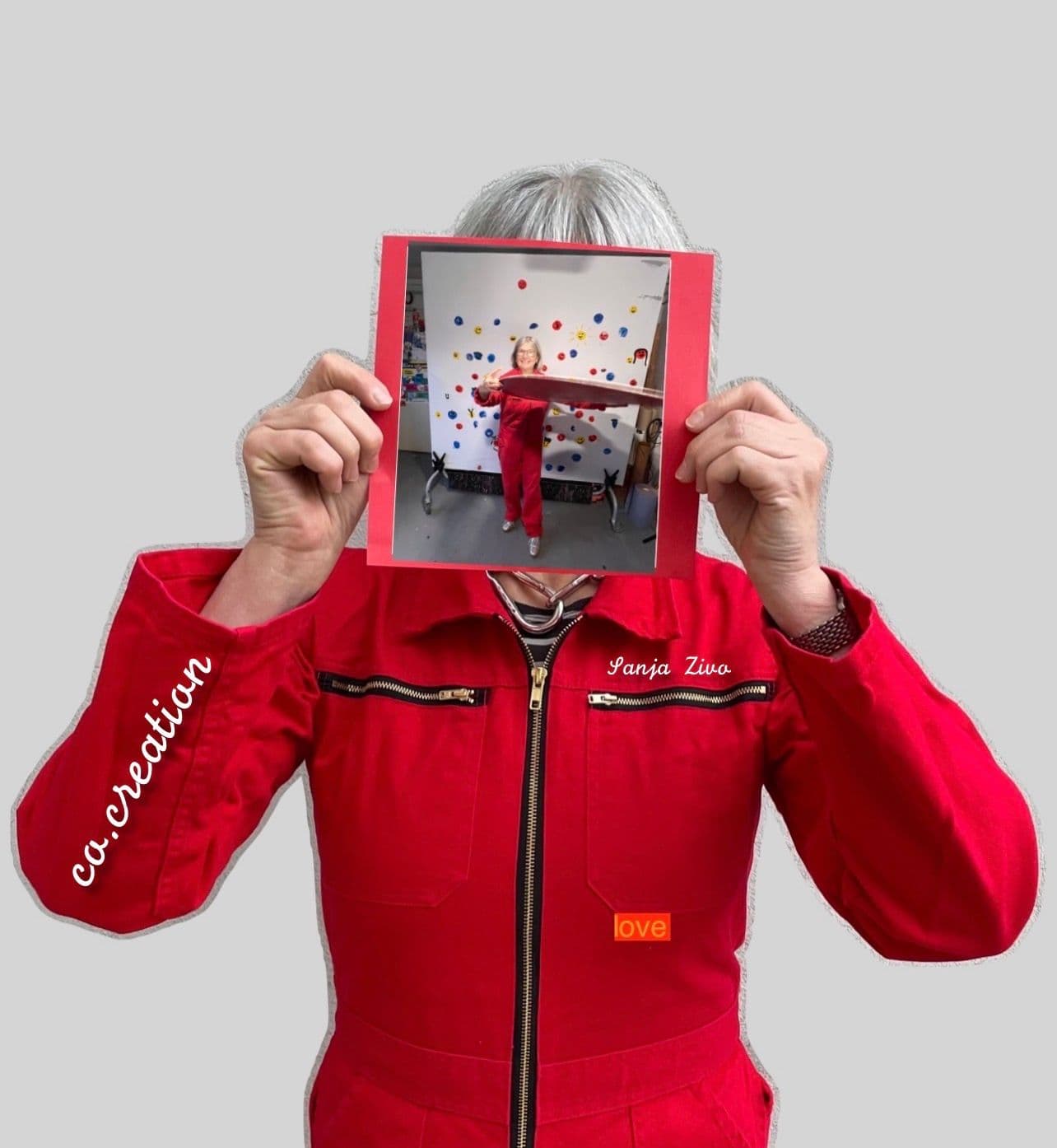 Eine Frau im roten Overall hält ein Bild vor ihr Gesicht