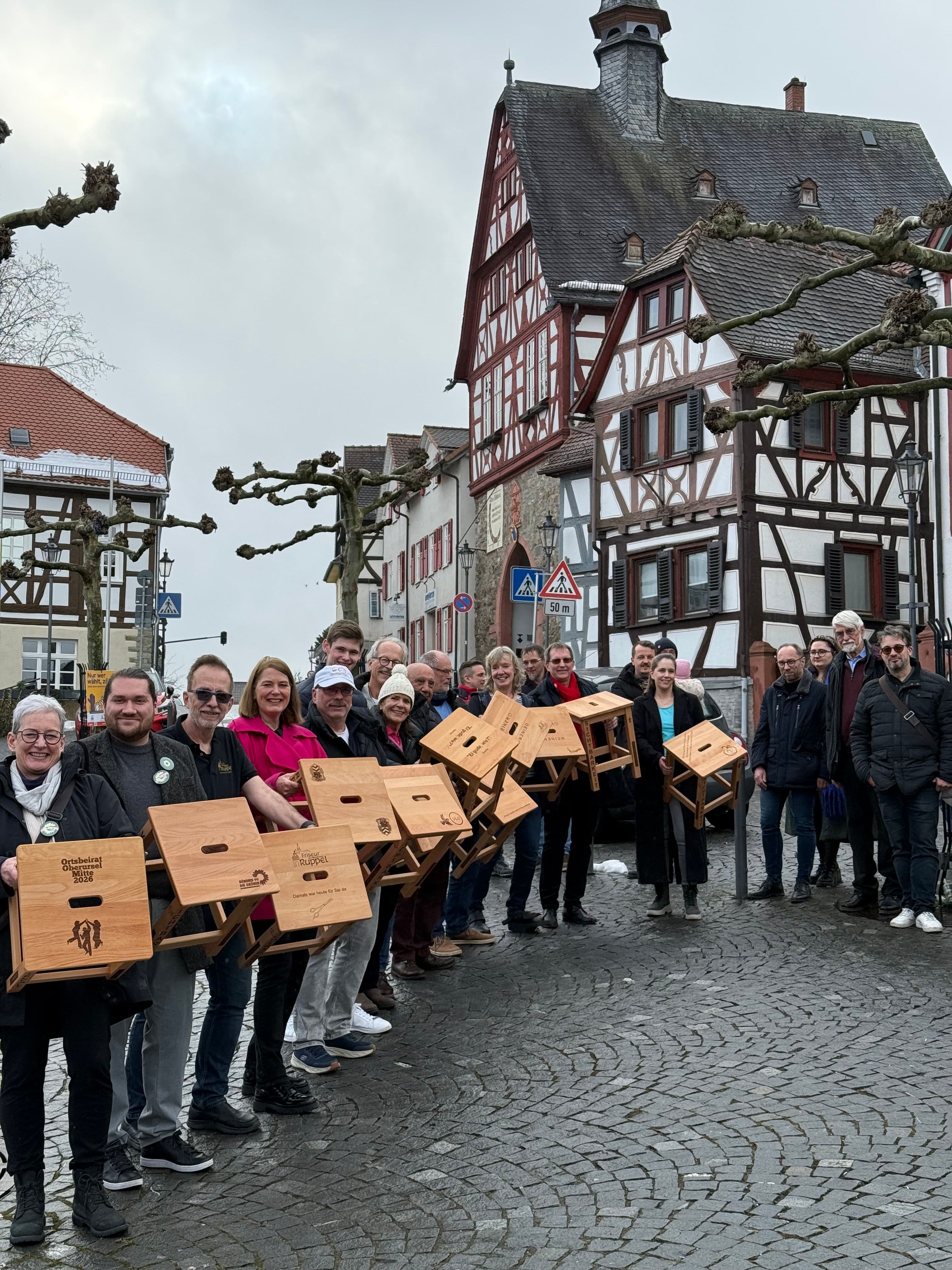 Mehrere Menschen stehen mit einem Holzkasten in der Hand auf dem Marktplatz Oberursel.