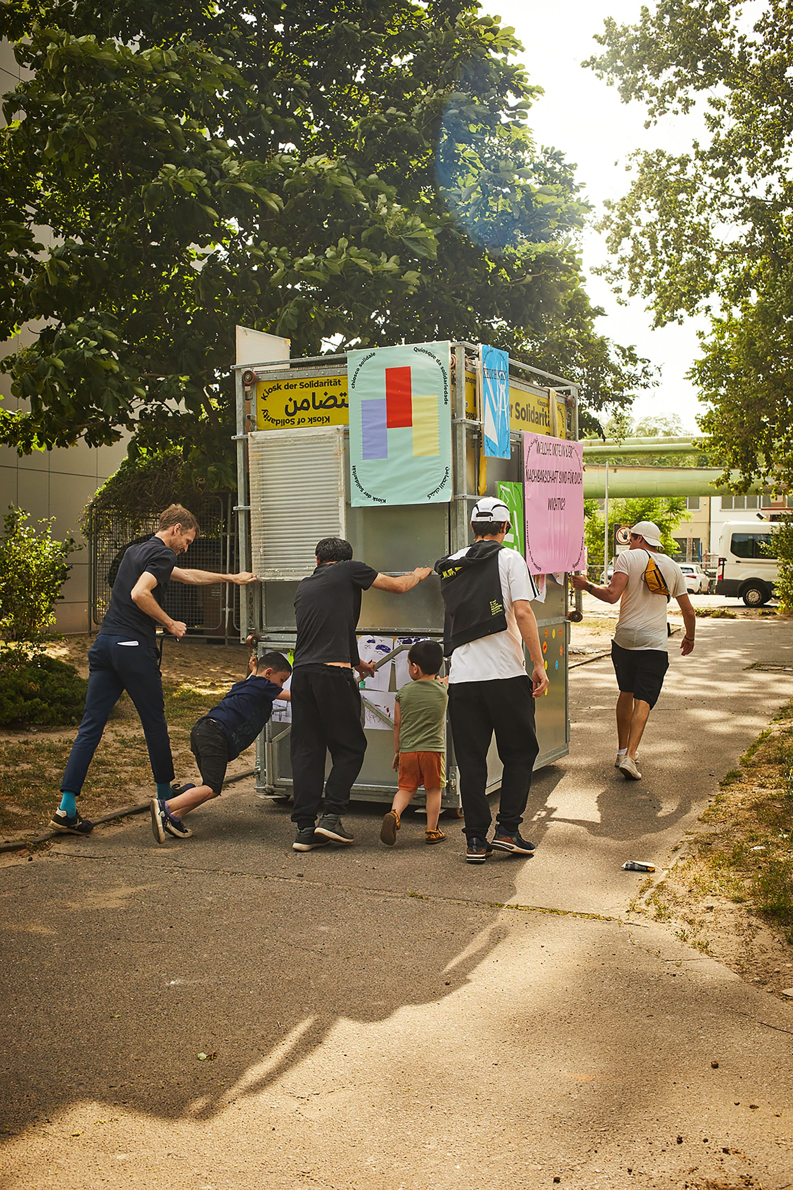 Mehrere Personen schieben einen mobilen Kiosk mit Plakaten.