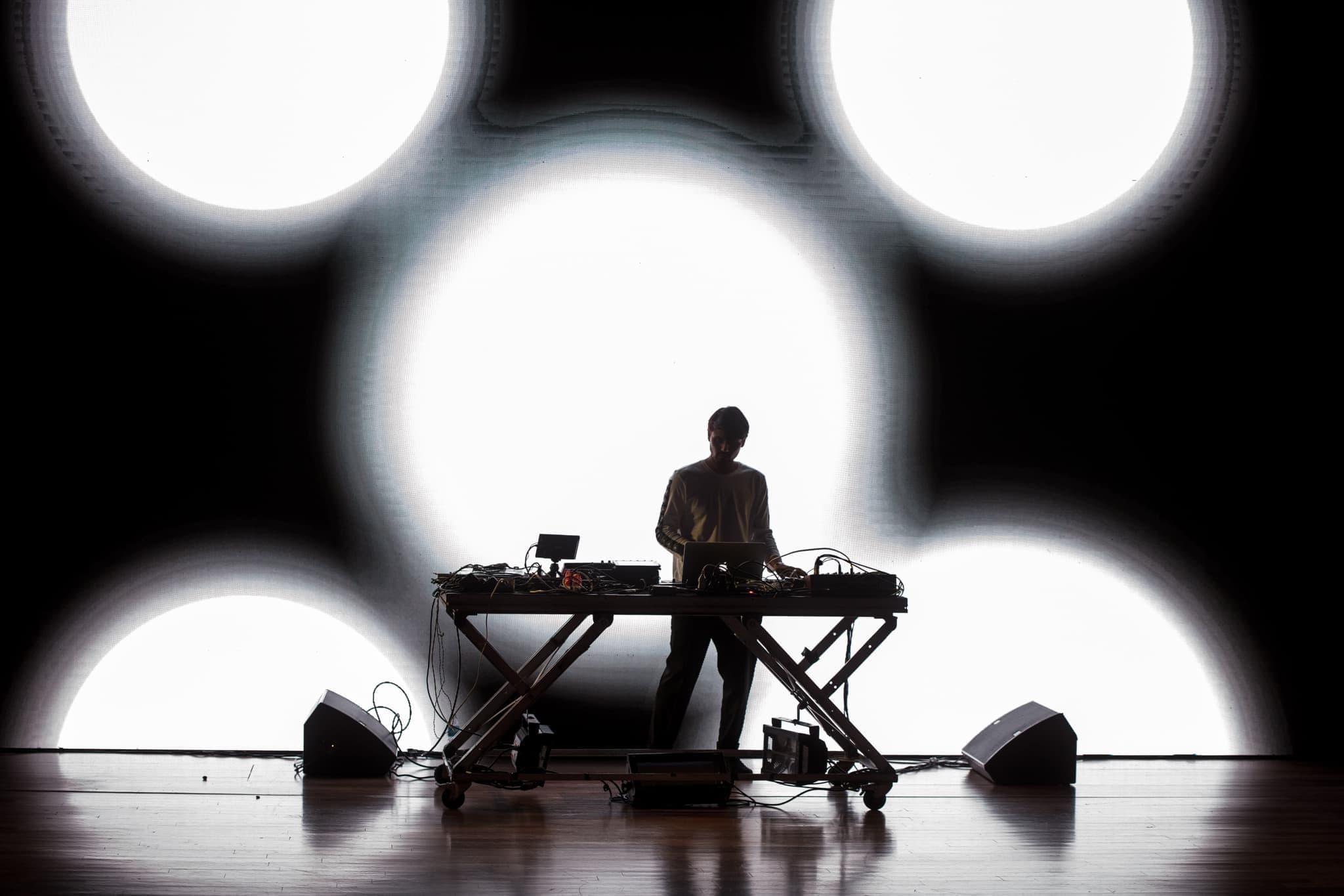 Eine Person hinterm DJ Pult und eine Lichtgrafik auf ihn projiziert 