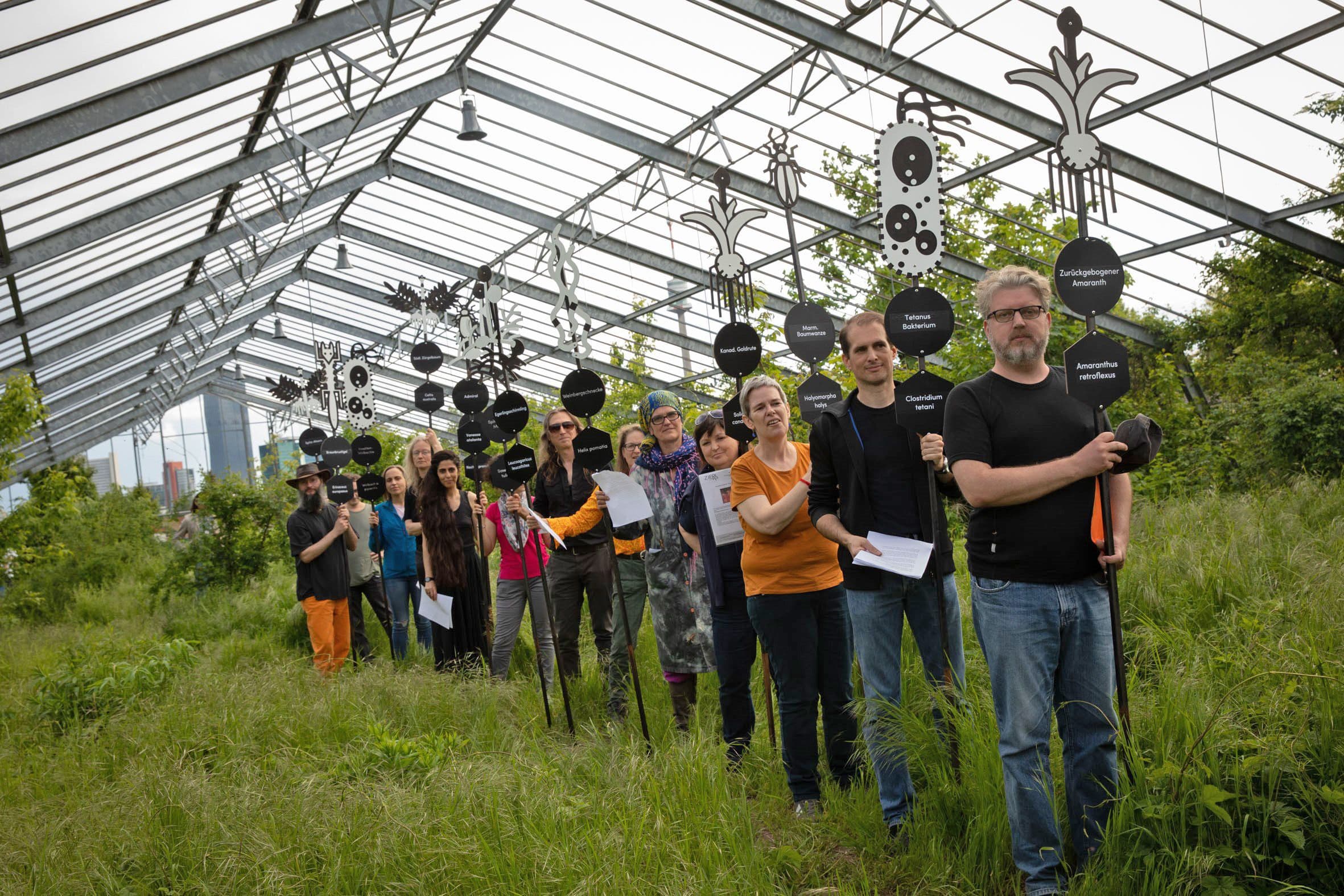 Menschen stehen mit Schildern in einem großen Gewächhaus