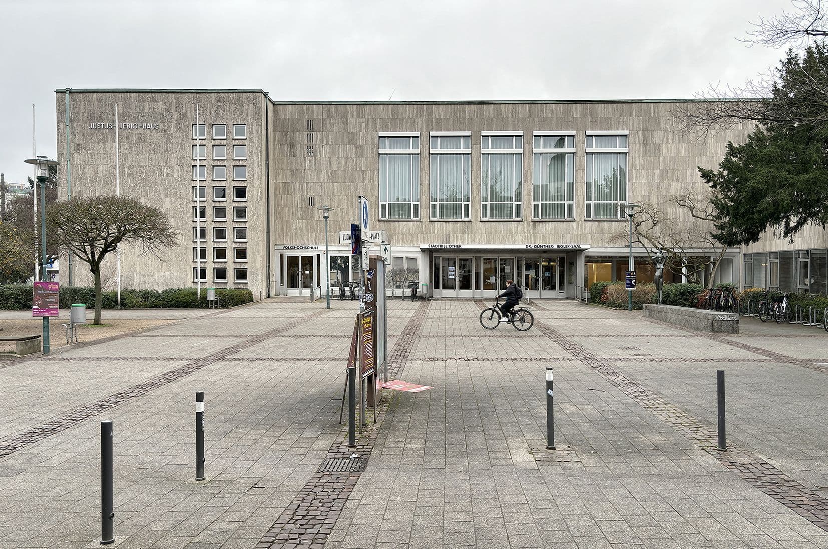 Ein Vorplatz führt zu einem großen, grauen Plattenbau: dem Justus-Liebig-Haus.
