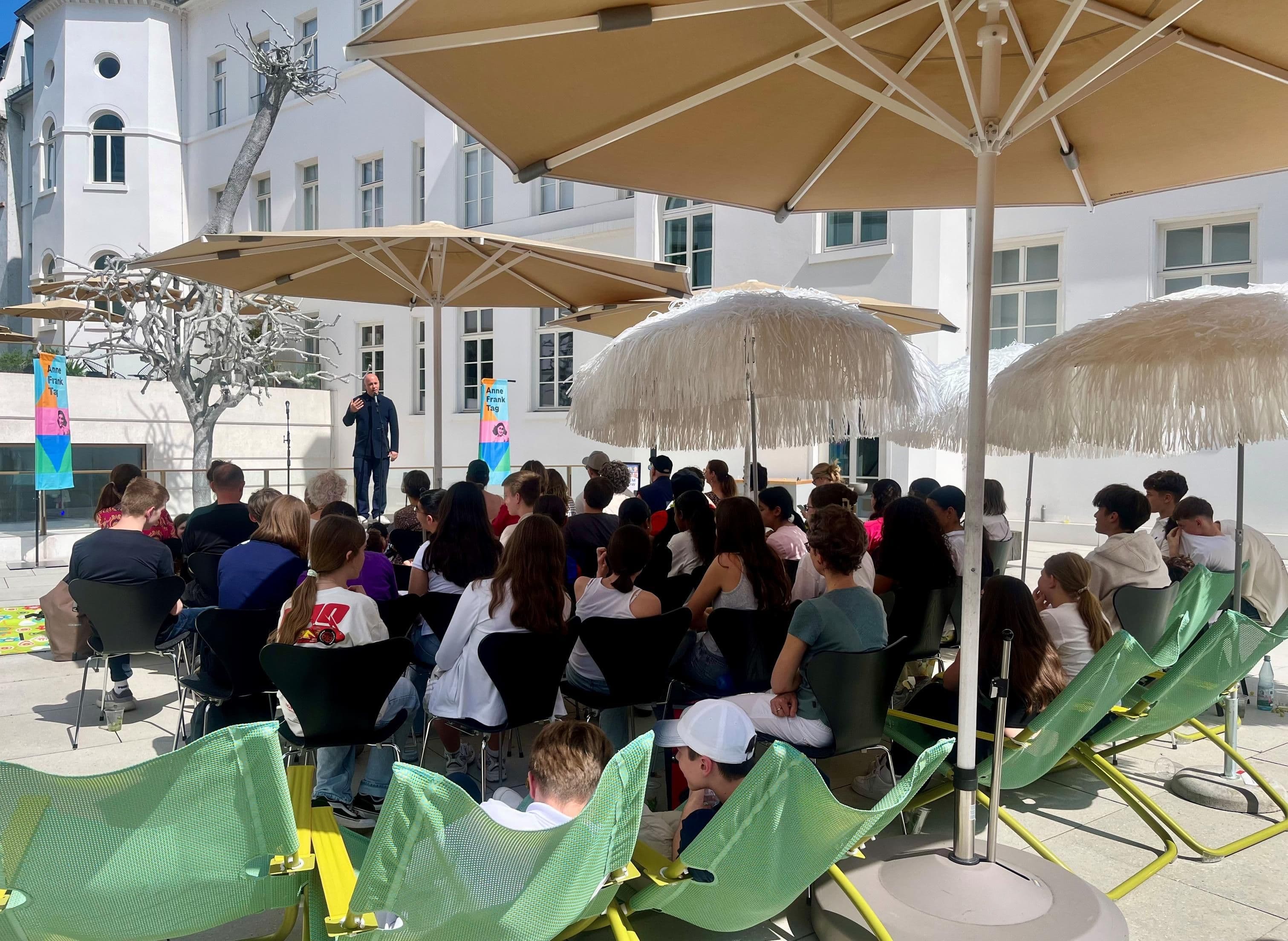 Menschen sitzen im Hof des jüdischen Museum und hören einem Redebeitrag zu