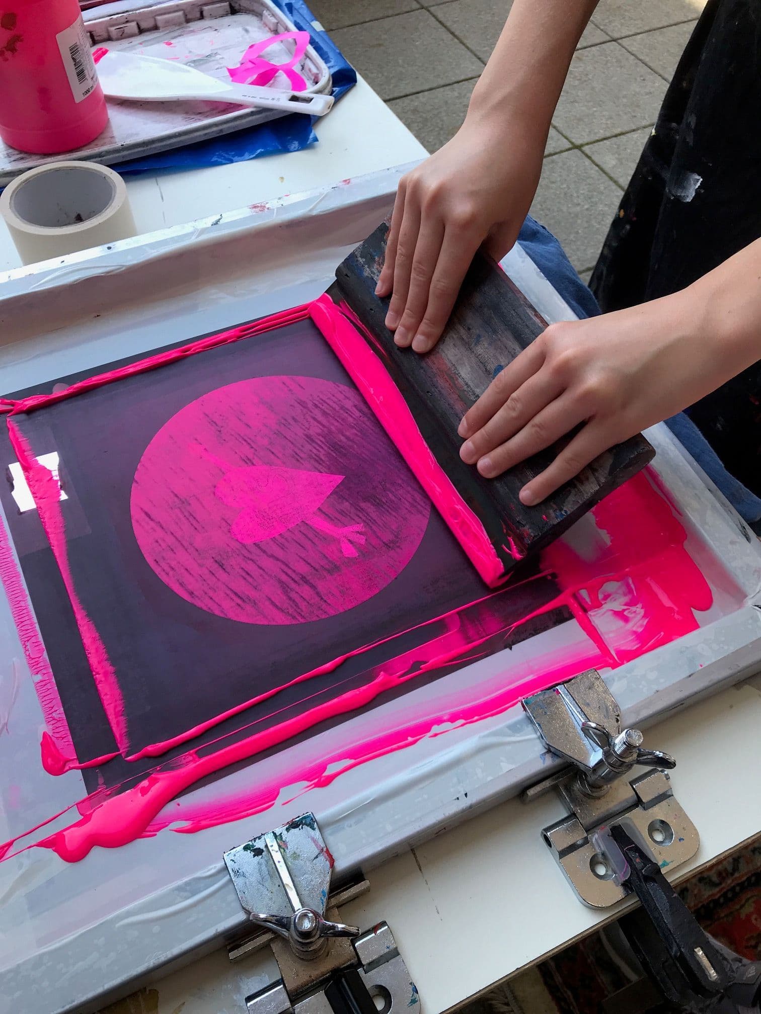 Mit knalliger pinker Farbe wird über eine Siebdruckplatte gestrichen.