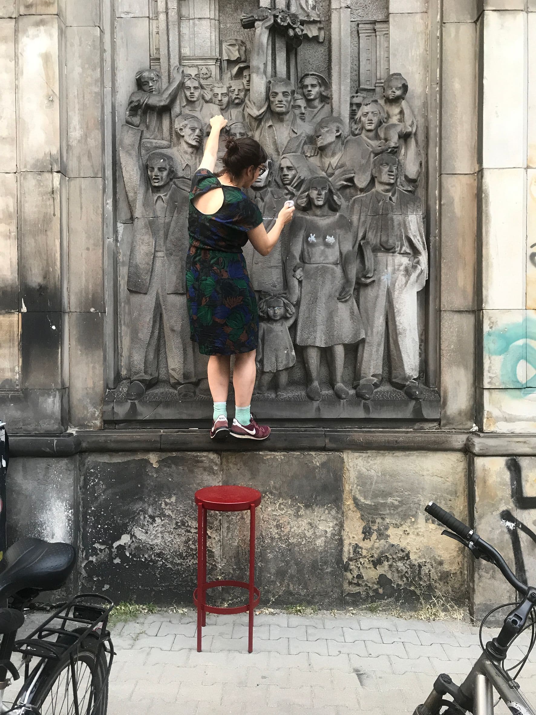 Eine Frau steht auf der Kante einer Gebäudewand und hält sich an Skulpturen in der Wand fest.