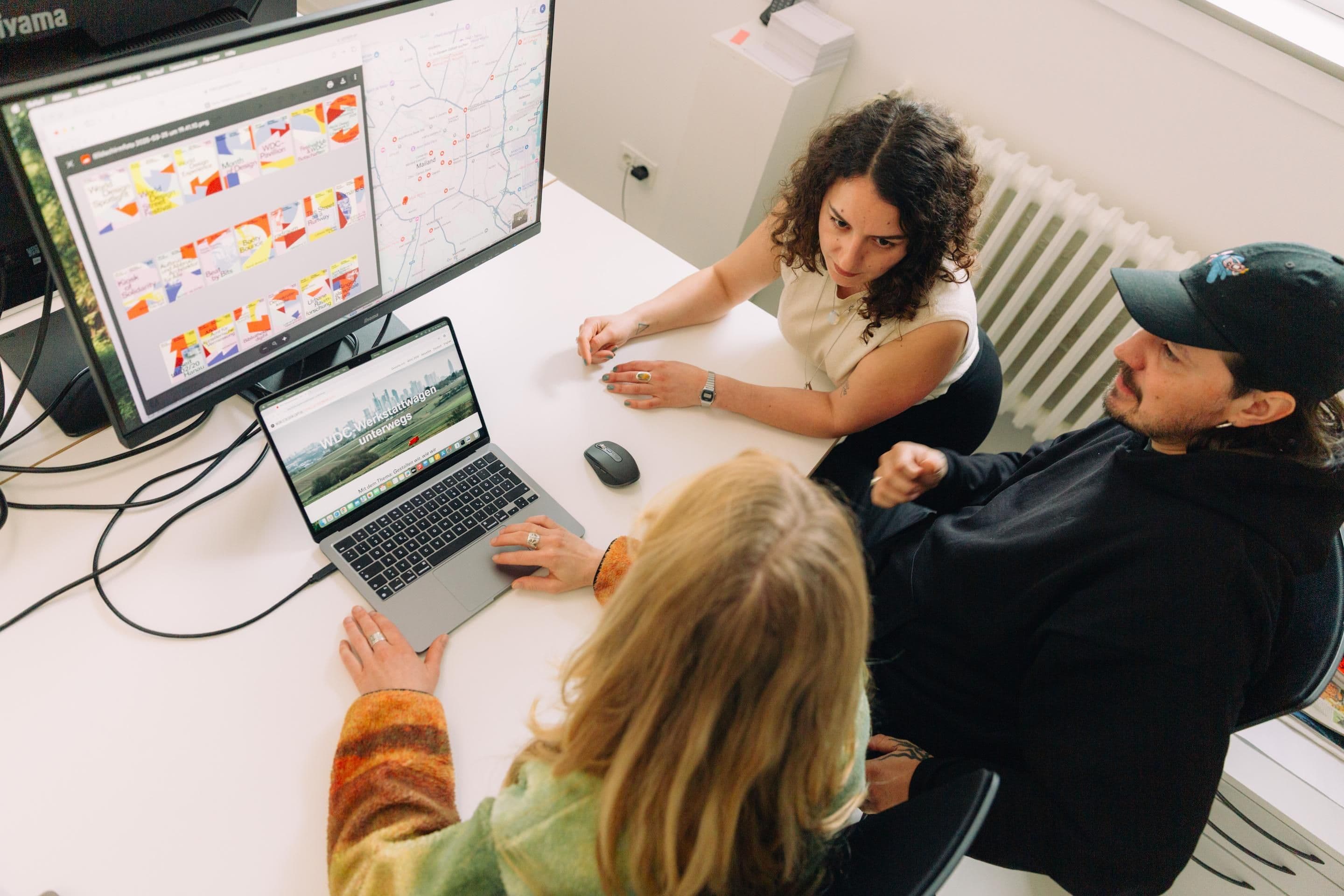 Drei Personen sitzen um einen Laptop herum und diskutieren.