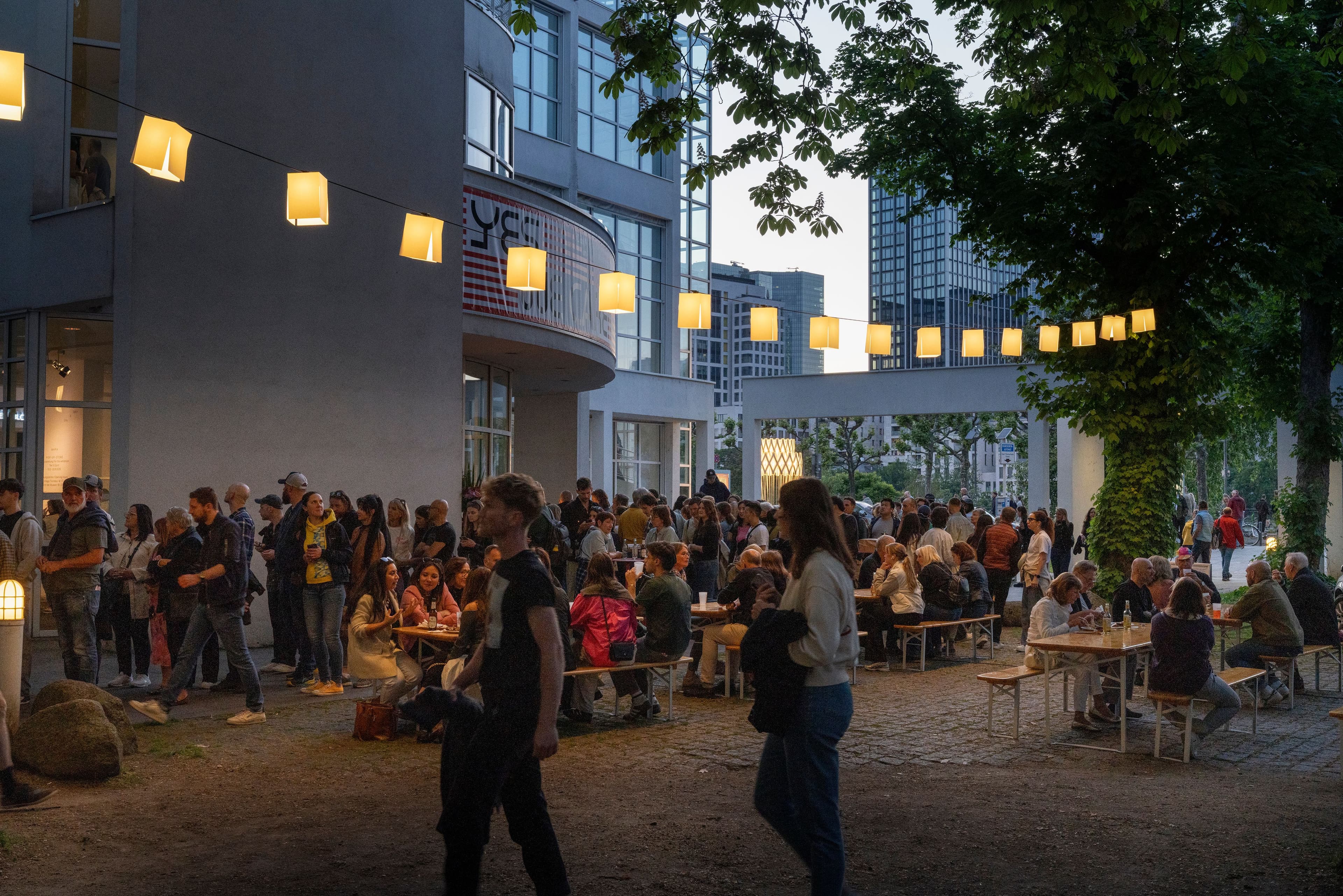 Menschen sitzen vor dem Museum Angewandte Kunst im Abendlicht