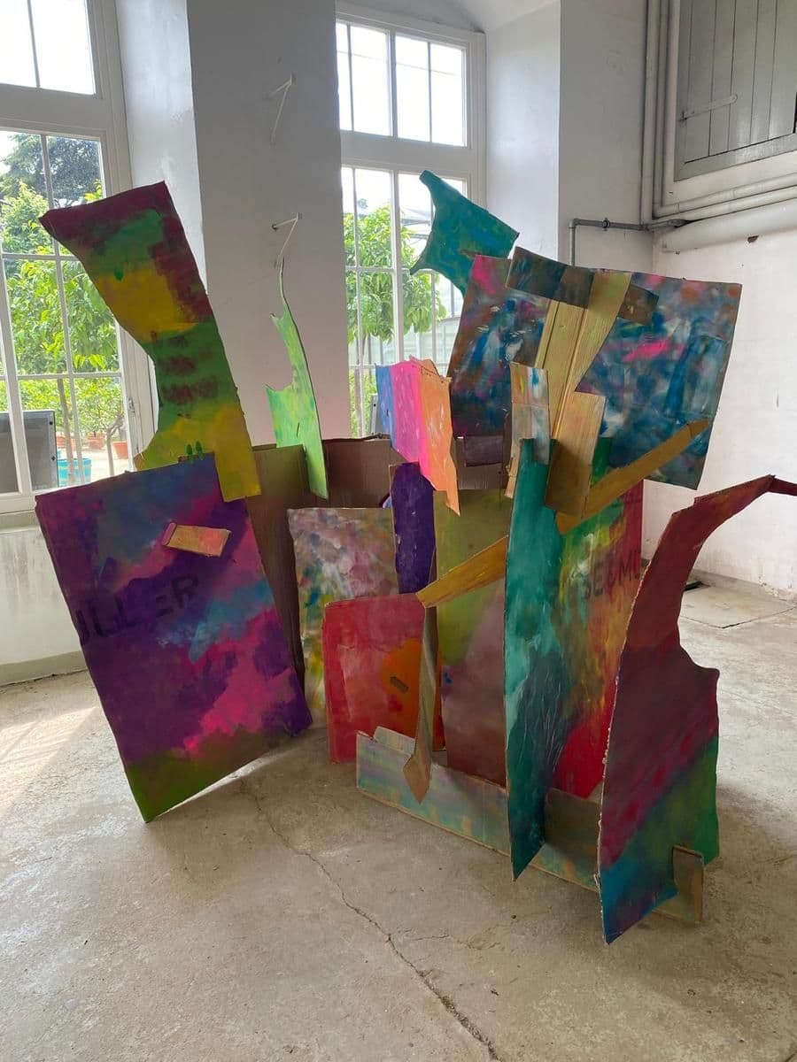 Bunte, abstrakte Skulpturen stehen in einem Raum mit vielen Fenstern.