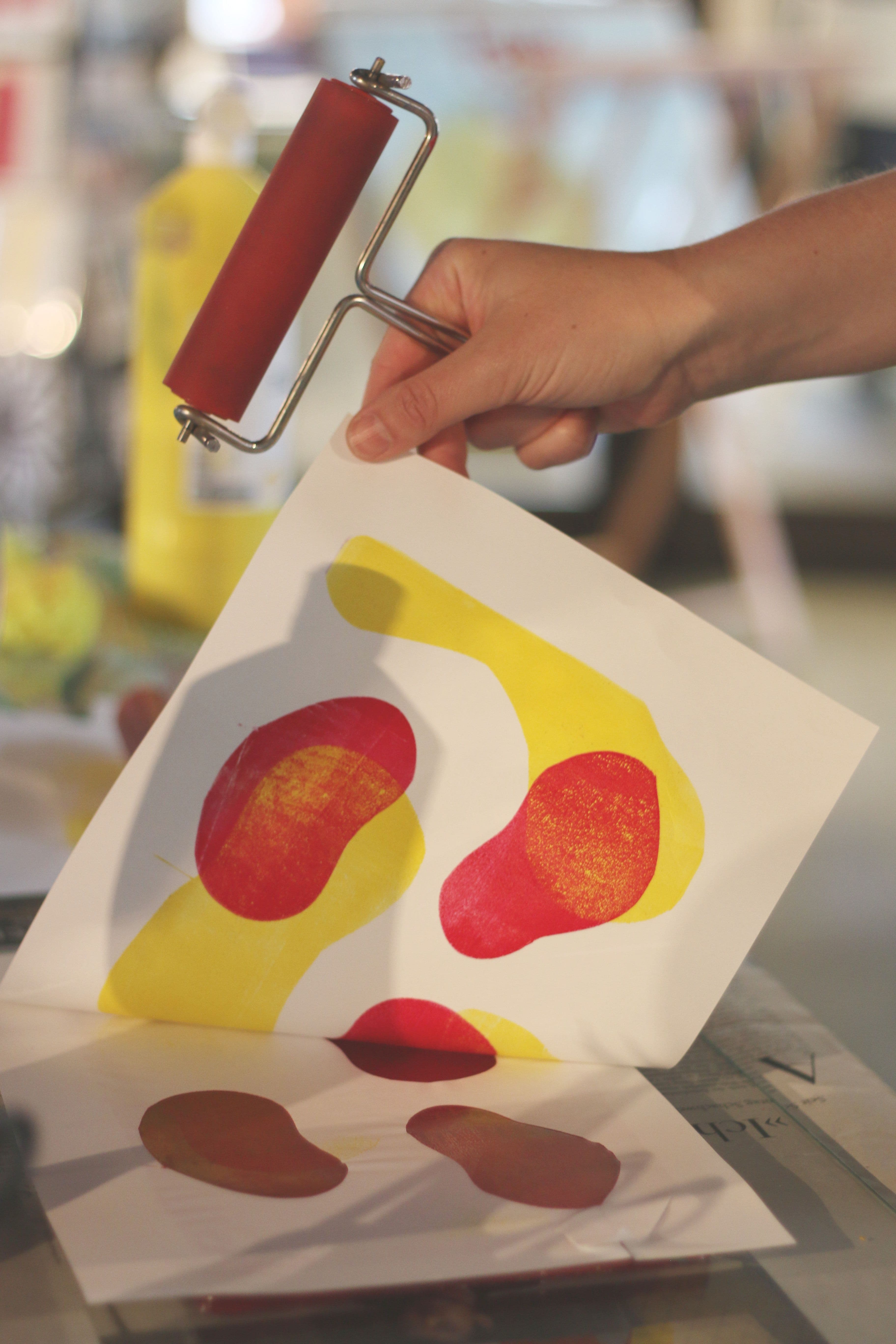 Eine Hand hält eine Linolrolle und hebt ein bedrucktes Blatt an.