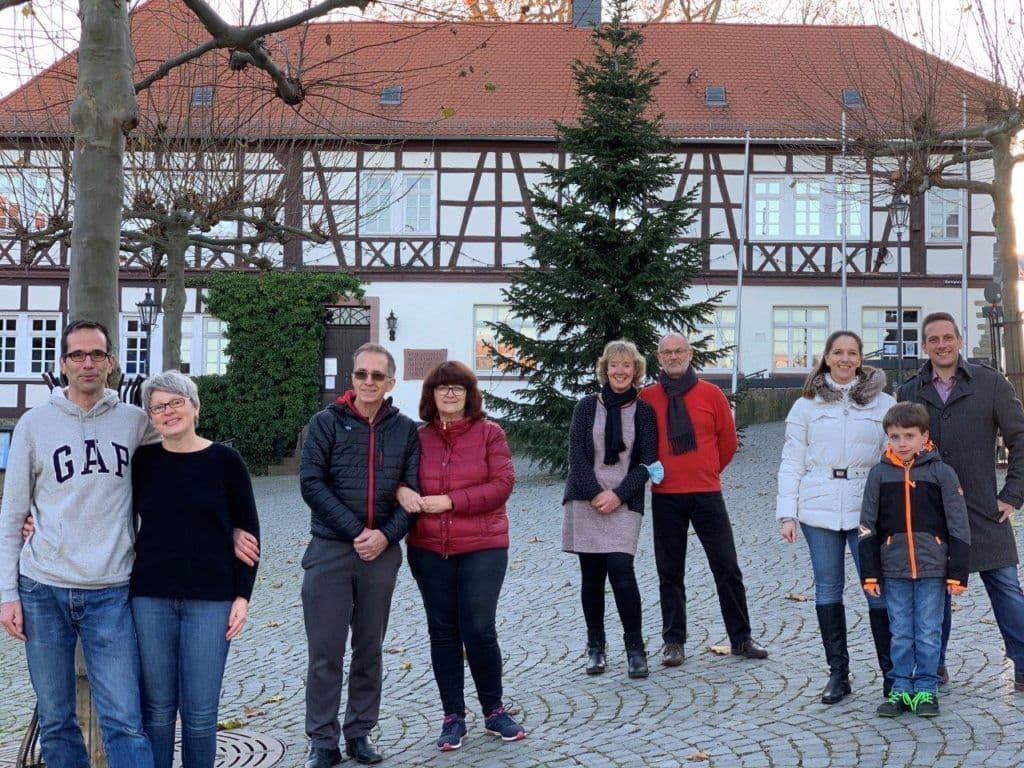 Auf einem gepflasterten Platz stehen neun Menschen, die alle in die Kamera schauen.