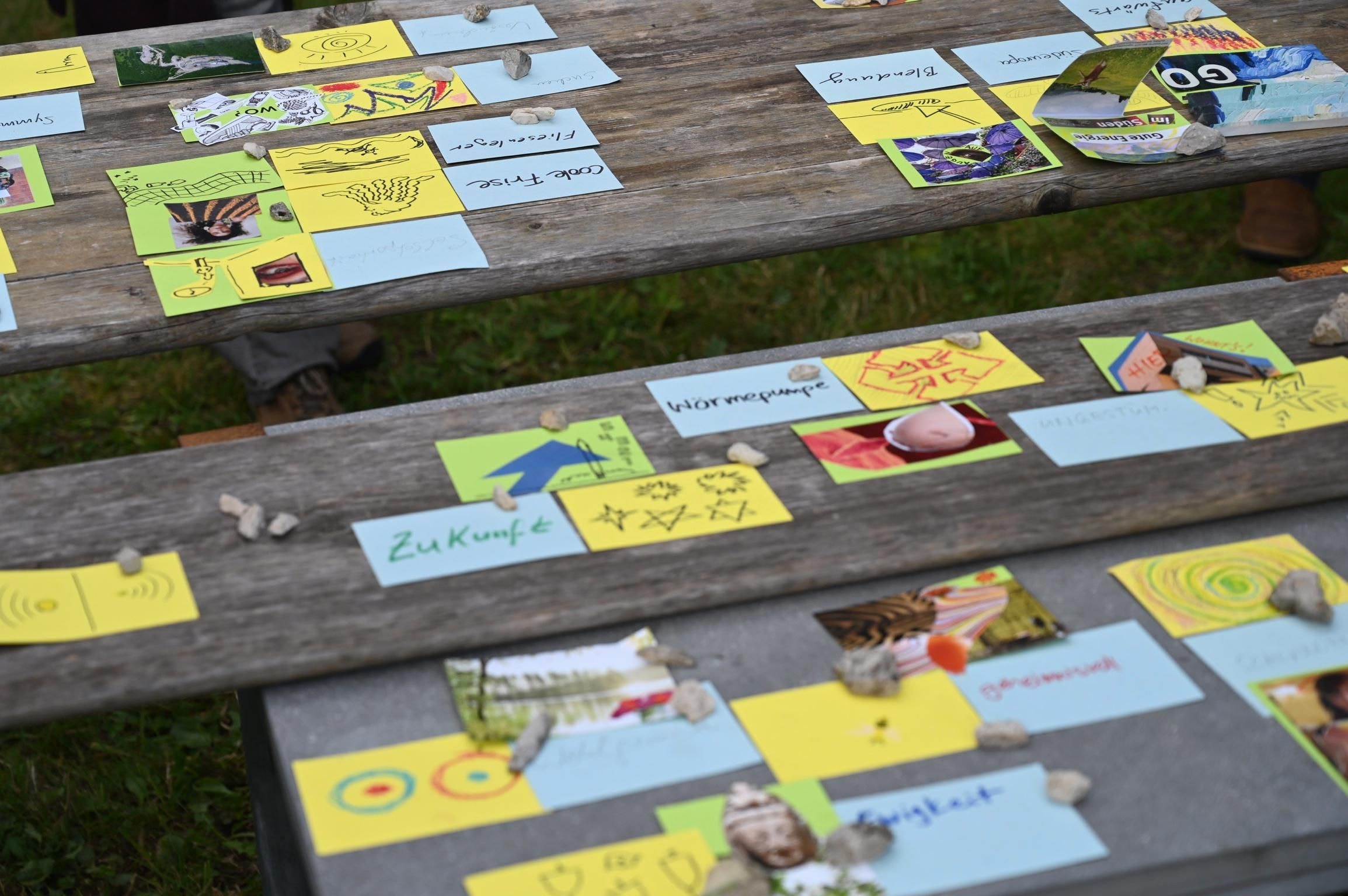 Auf einem Holztisch liegen mehrere bunte Karten, Fotos und Notizzettel.