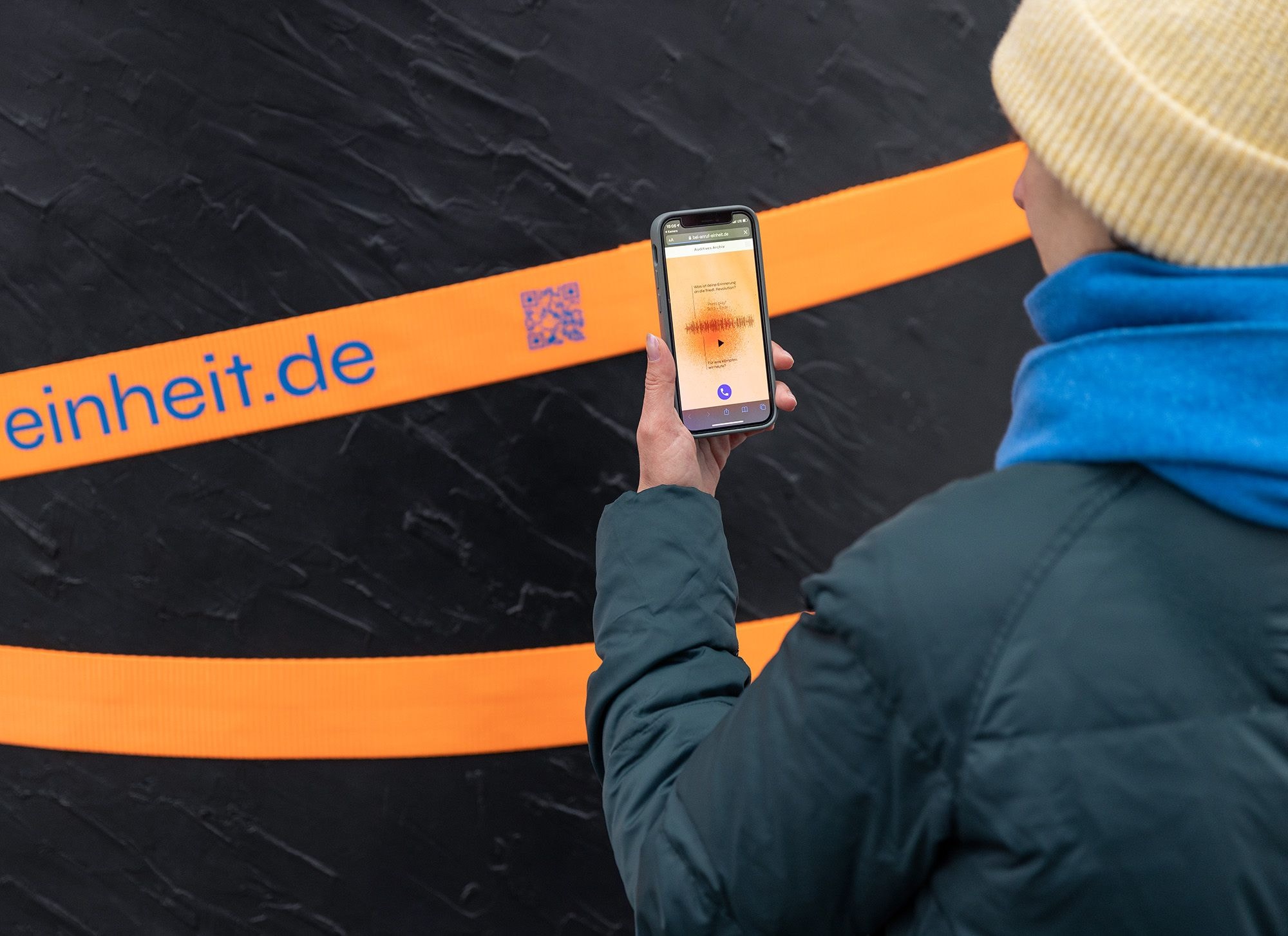 Person mit Handy scannt ein orangenes Band 