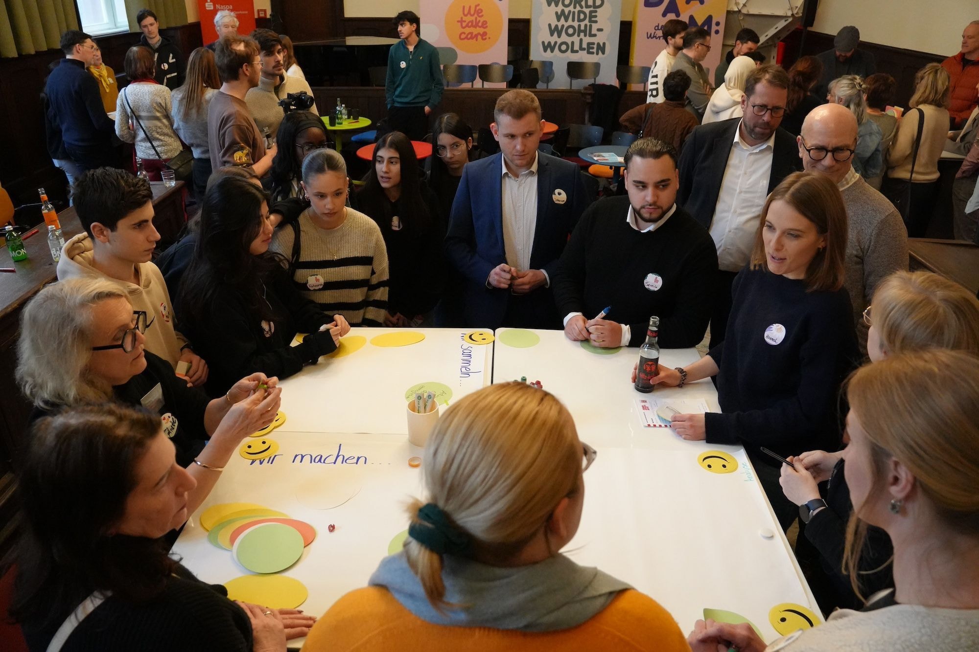 Verschieden Menschen stehen um einen Tisch und unterhalten sich.