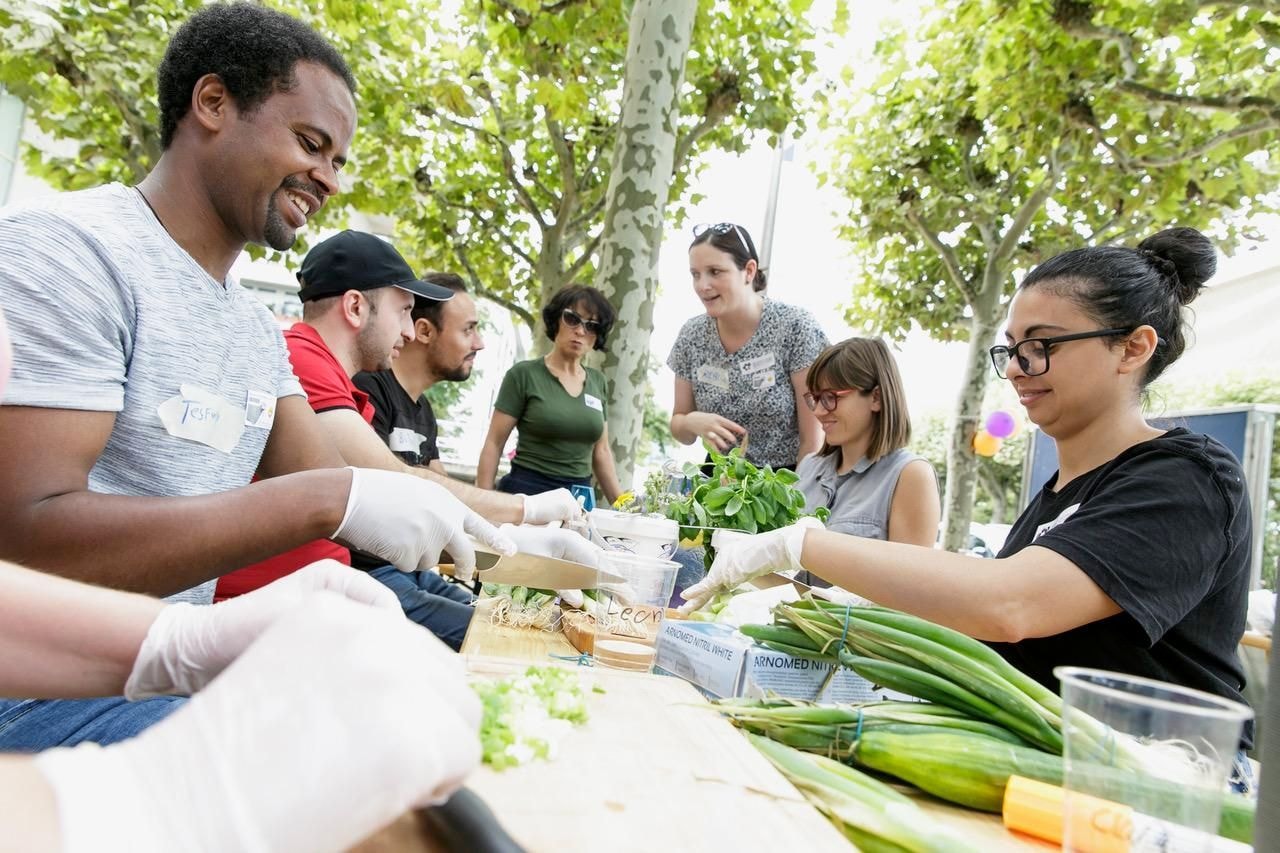 Mehrere unterschiedliche Personen sitzen zusammen an einem Tisch und kochen.