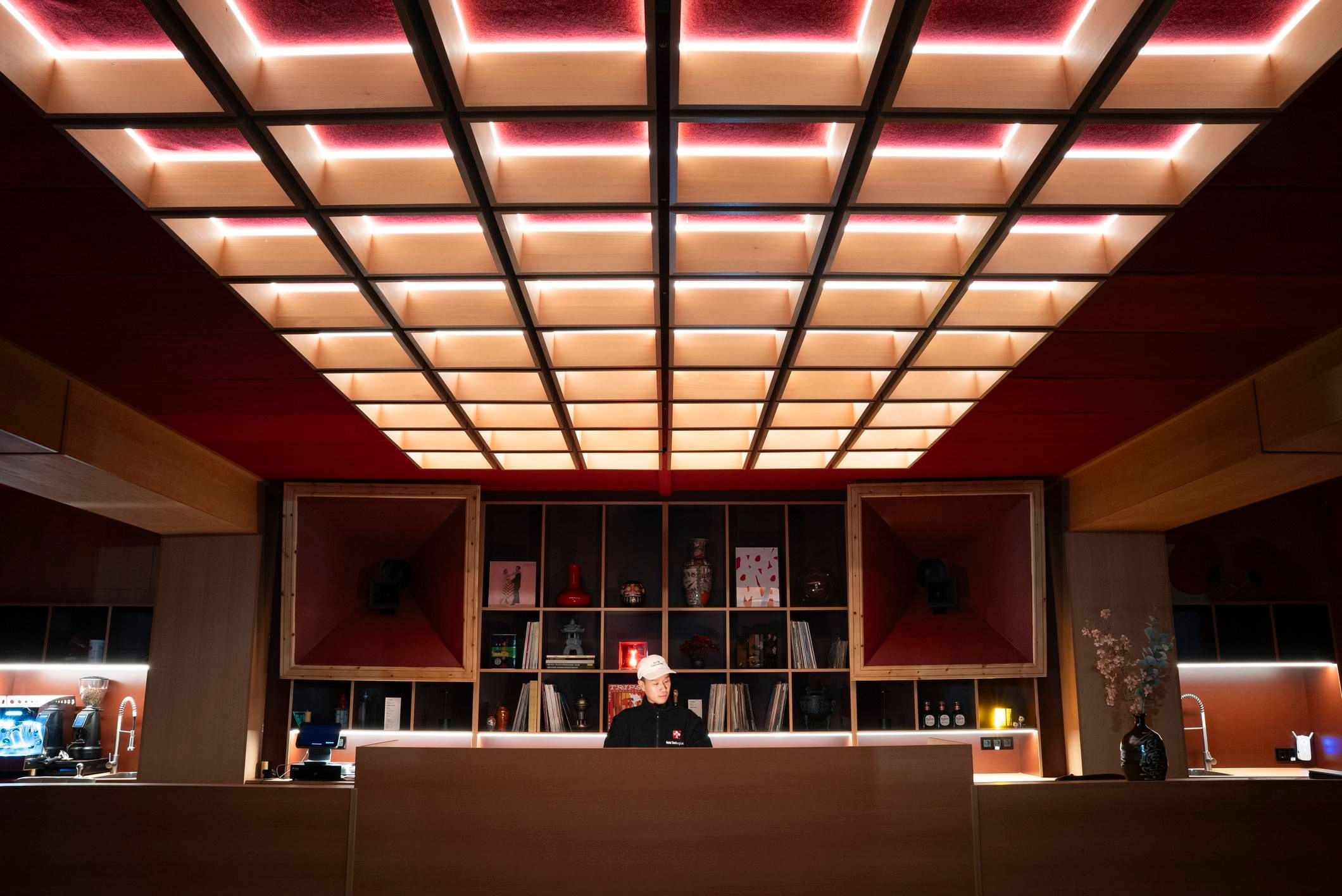 Ein Mann steht hinter einer großen schönen Bar. Die Decke des Clubs ist eindrucksvoll beleuchtet.