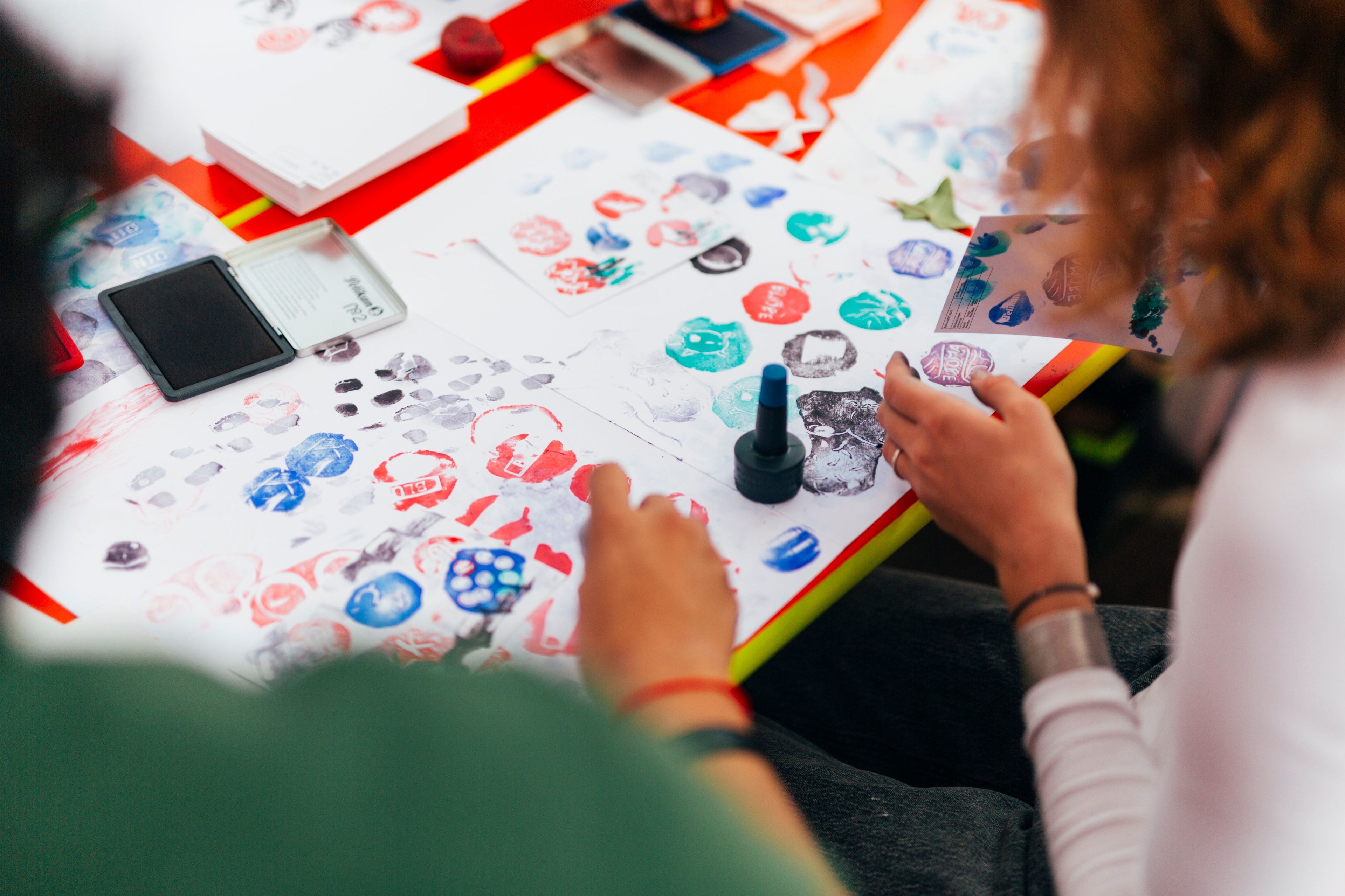 Zwei Personen stempeln mit Farben auf ein Blatt Papier