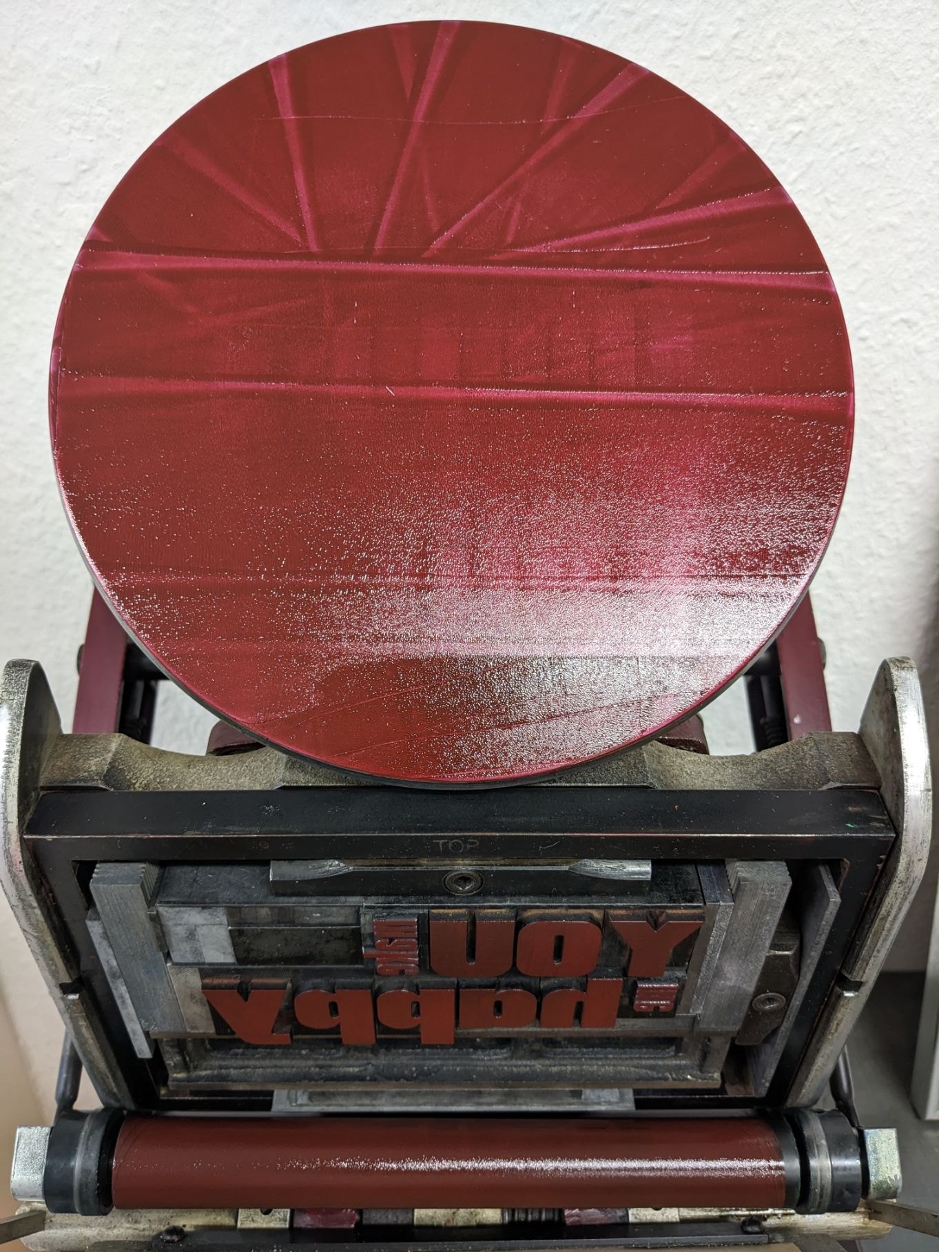 Eine rot eingefärbte runde Platte liegt auf einer Druckmaschine.