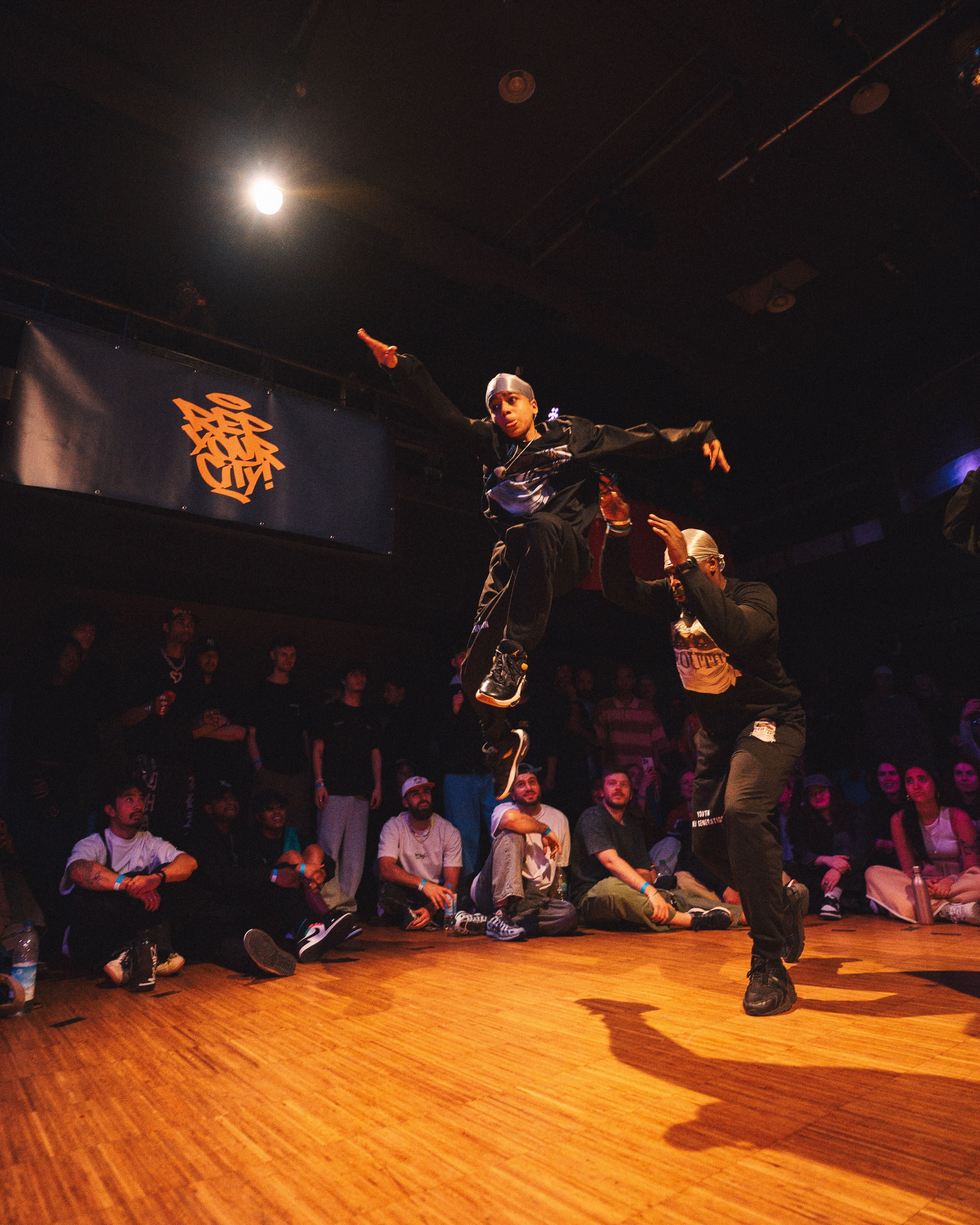 Ein Junge und ein Mann führen in einem Raum vor Publikum eine akrobatische Tanzvorstellung auf.