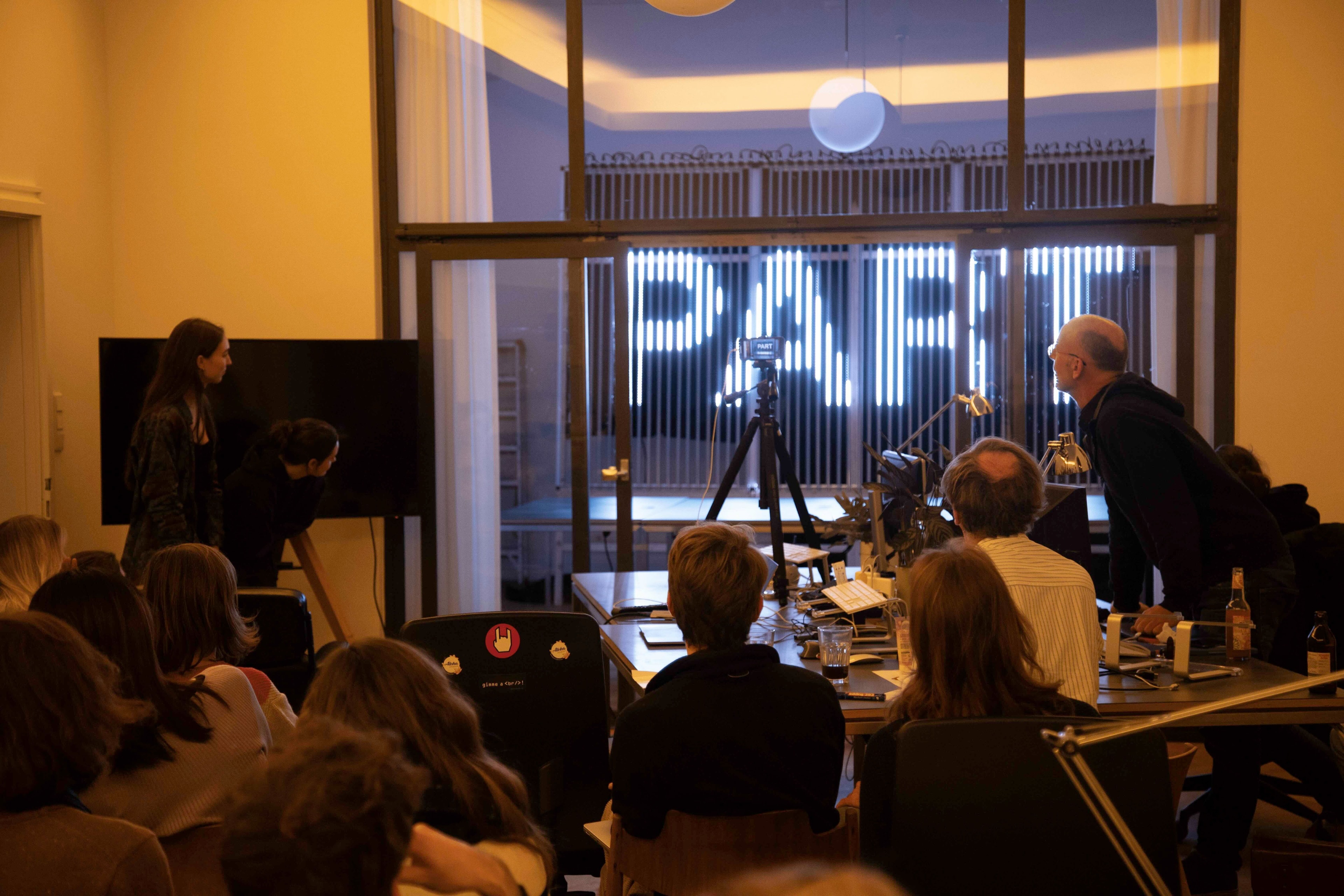 In einem Raum schauen verschiedene Leute auf eine LED-Schrift-Installation.