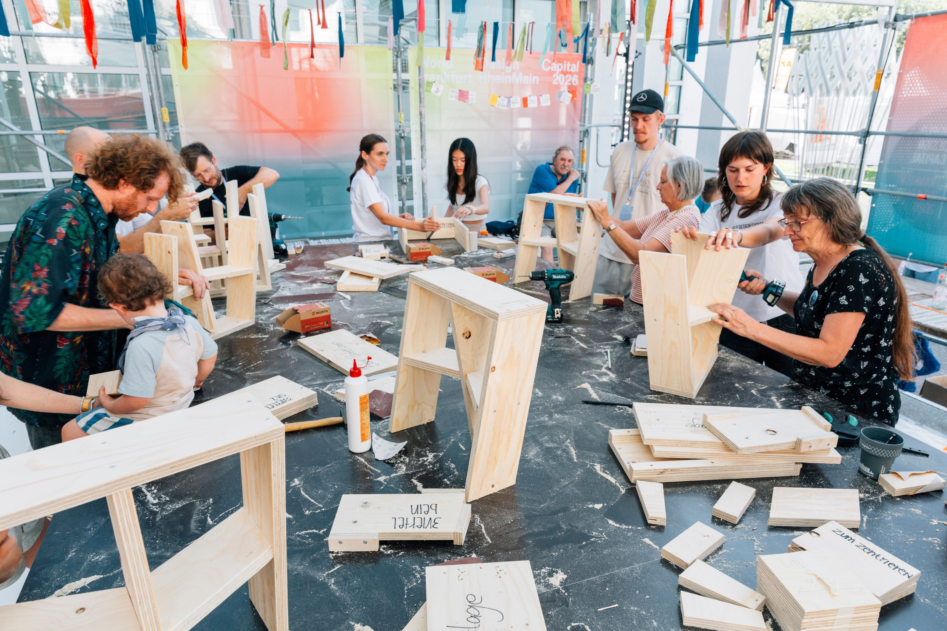 Menschen bauen Holzhocker bei einem Workshop von WDC 2026