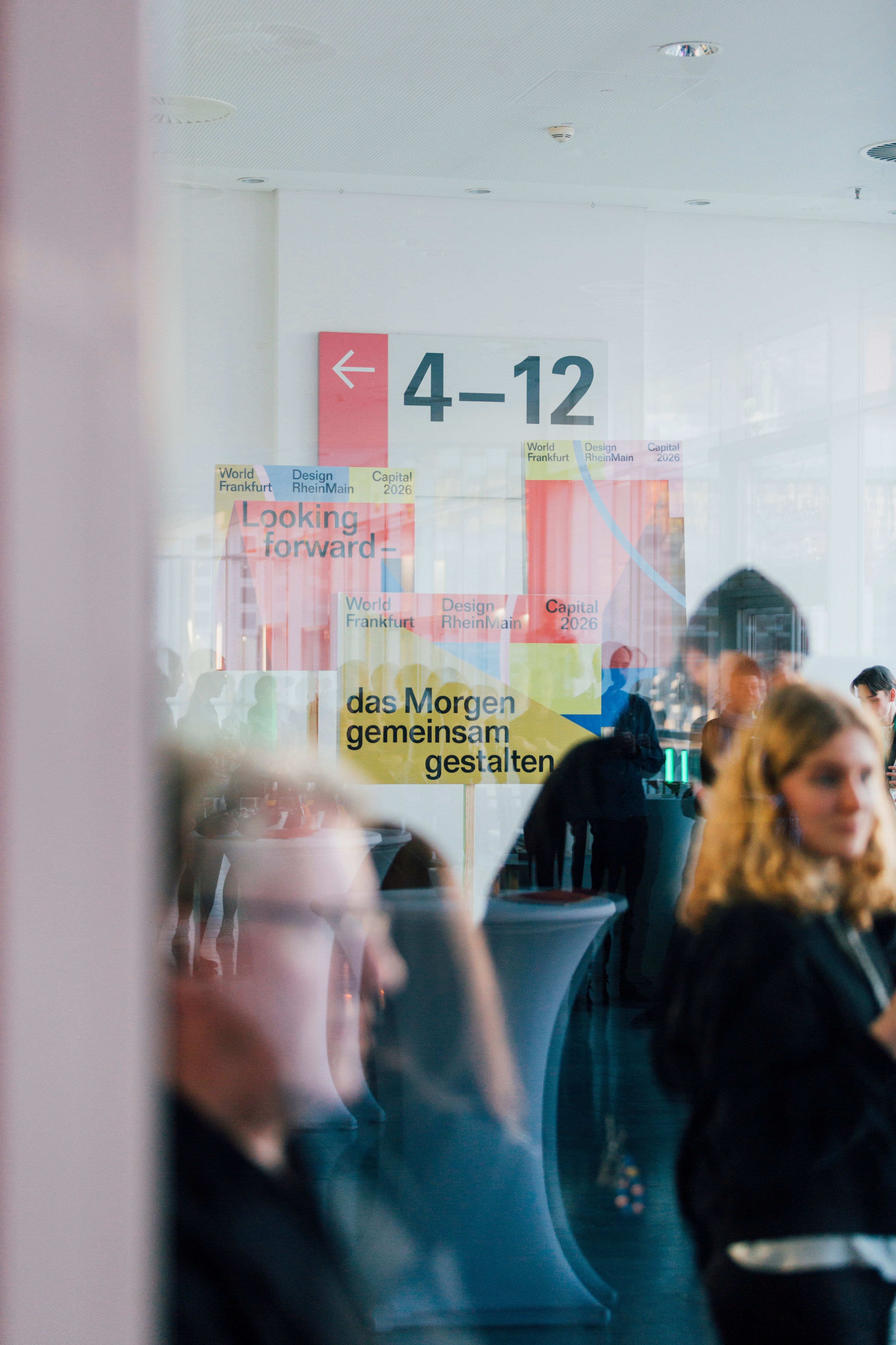 Menschen im Vordergrund und im Hintergrund sieht man Plakate von WDC 2026