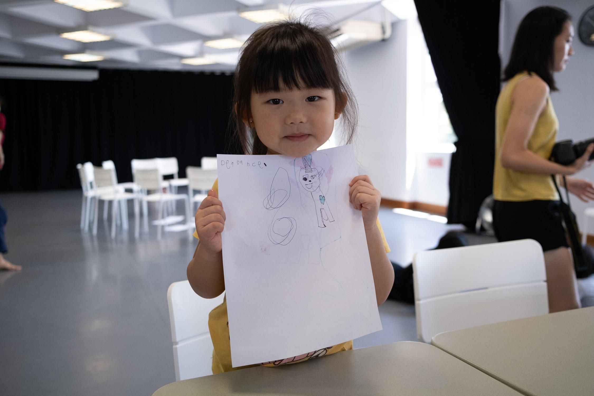 Ein kleines Kind hält ein Blatt Papier mit einer Zeichnung vor sich.