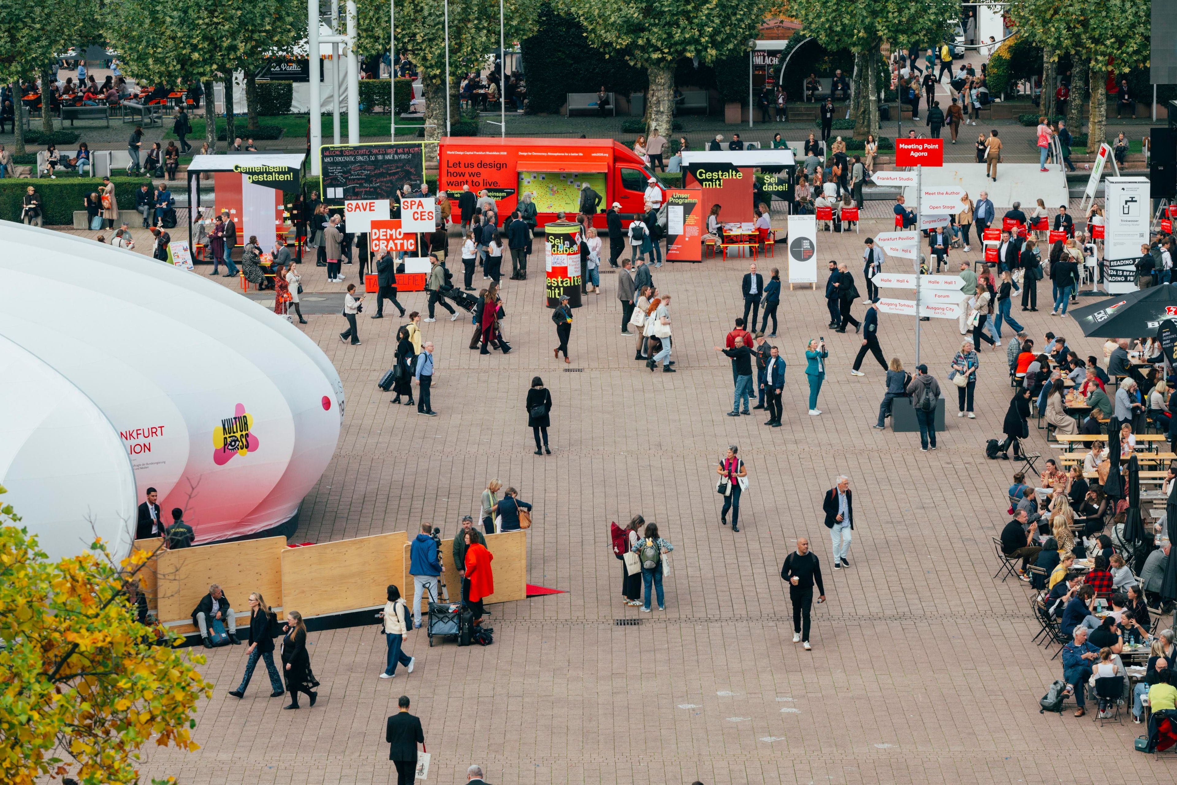Menschen sind auf dem Platz vor der Messe Frankfurt. Im Hintergrund steht der rote Werkstattwagen von WDC 2026.