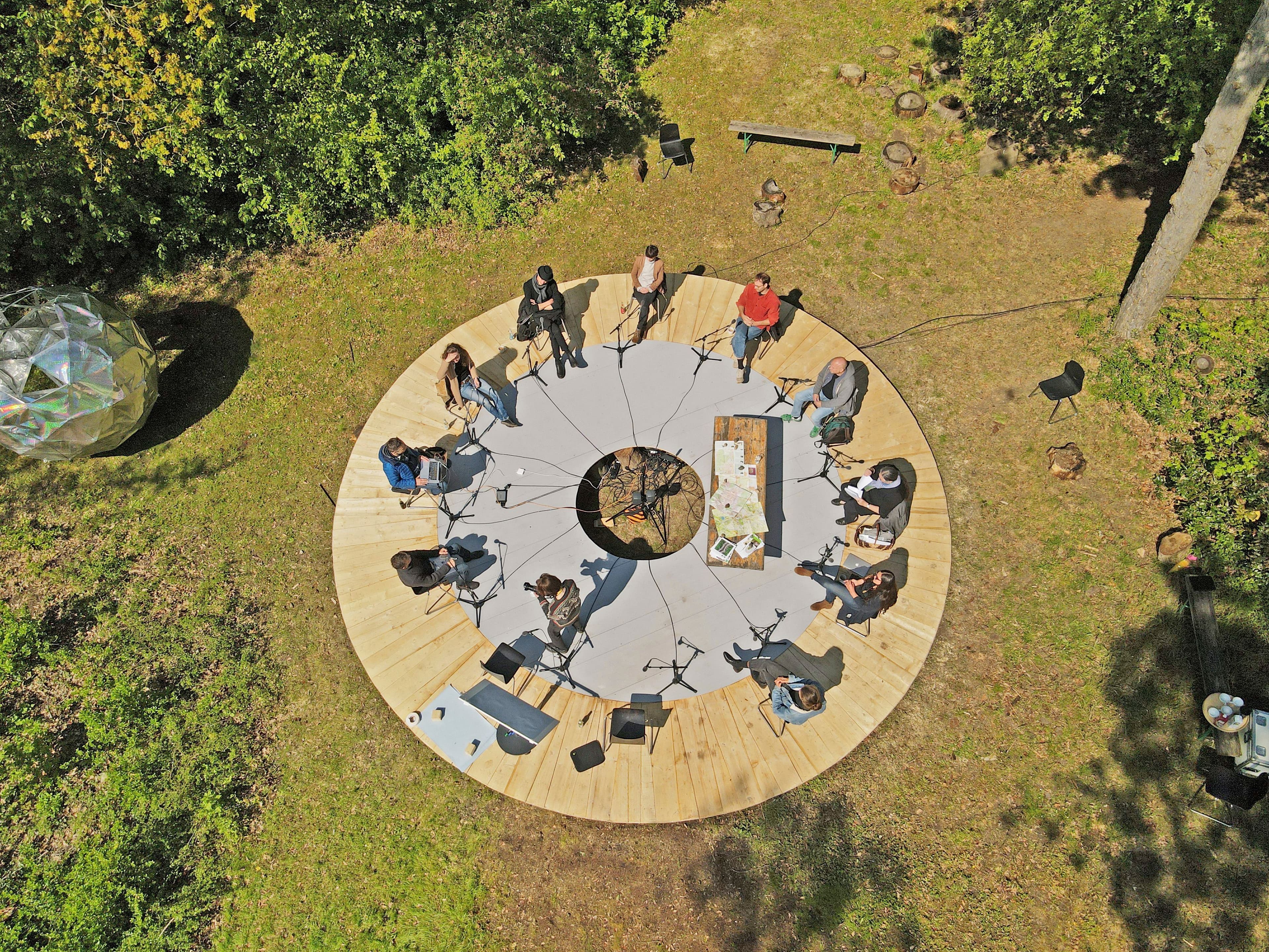 Menschen sitzend auf einer runden Holzplattform im Grünen