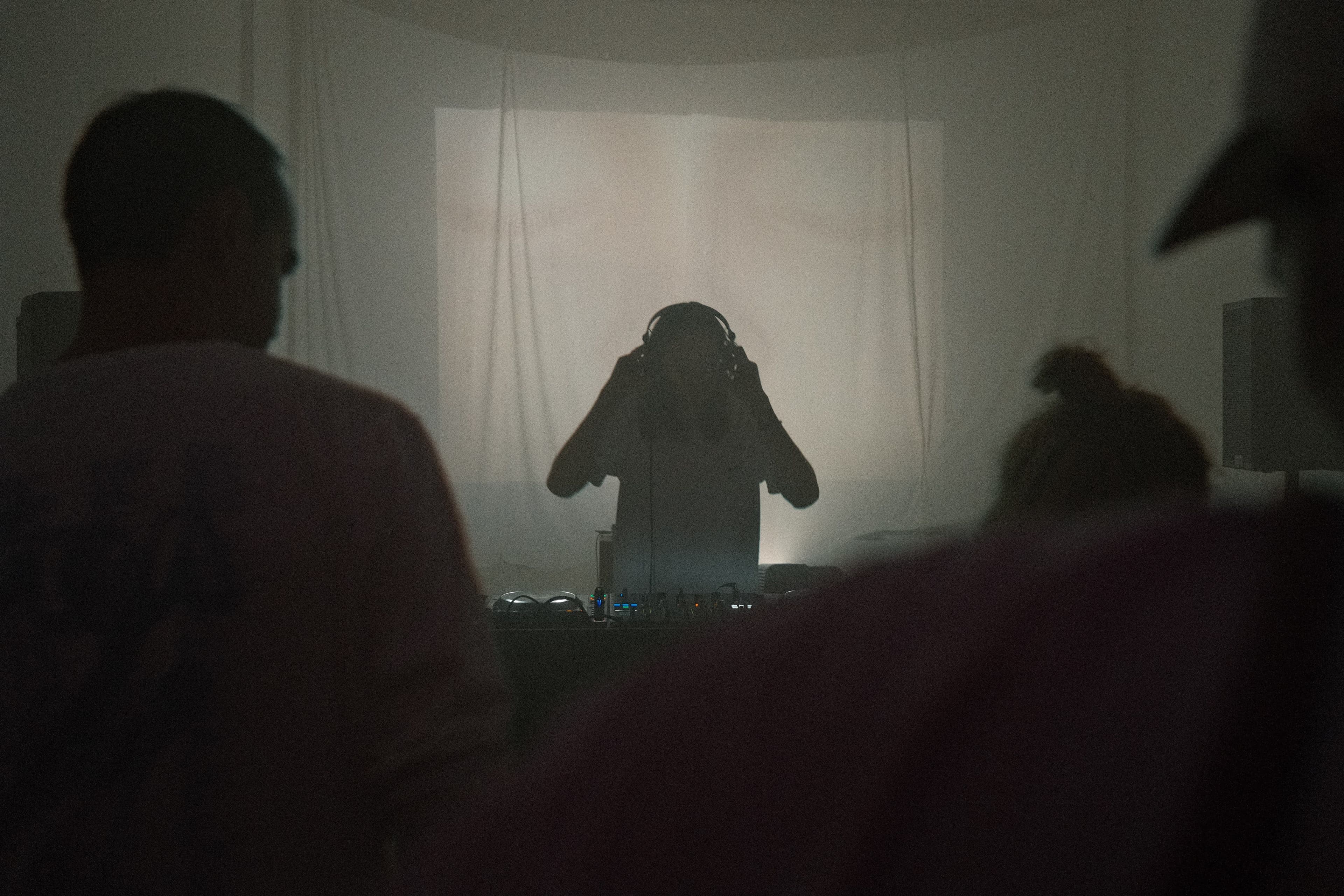 Ein verdunkelter raum mit nebel und einer Person am DJ Pult
