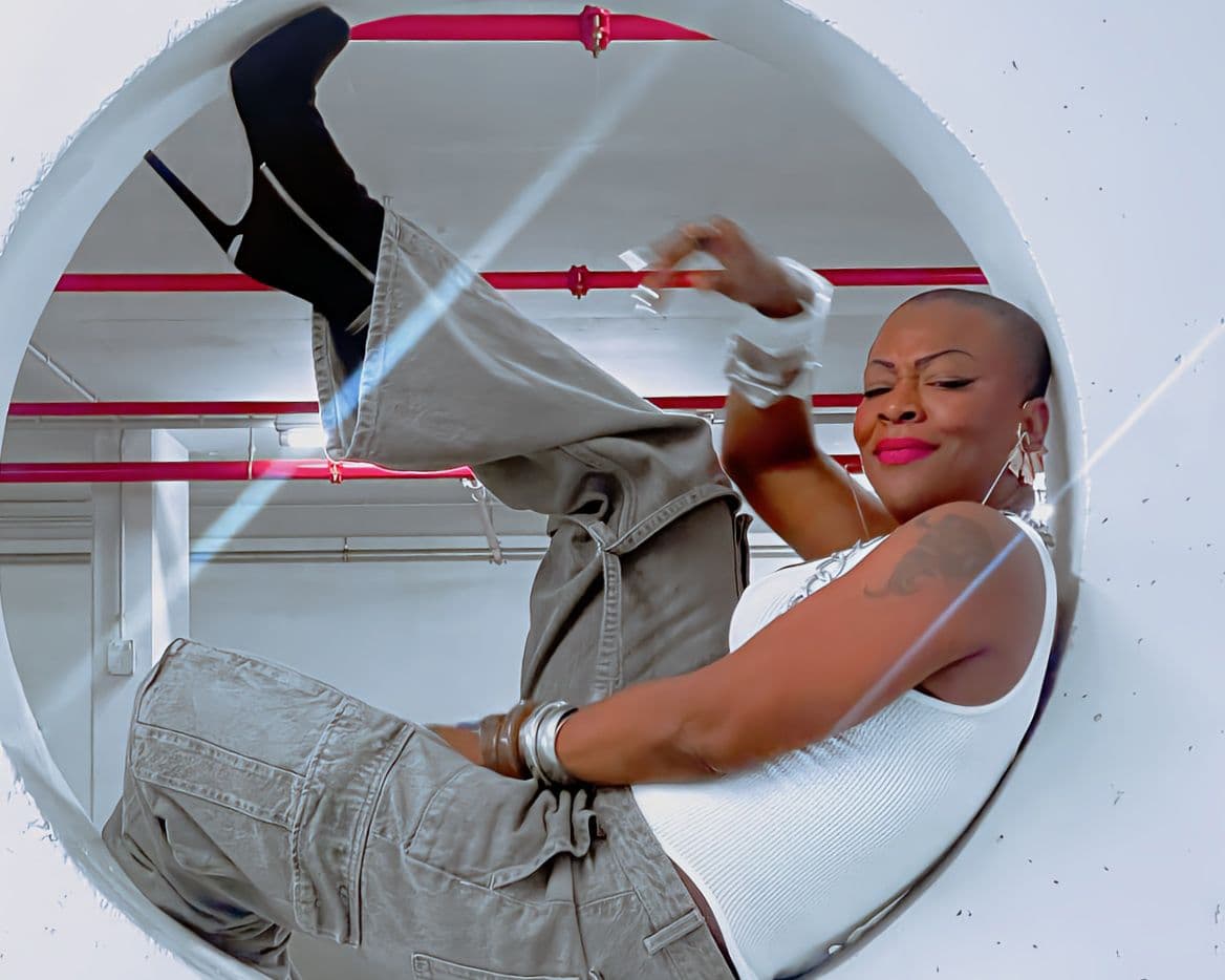 Eine Künstlerin sitzt in einer kreisrunden Öffnung und guckt selbstbewusst in die Kamera