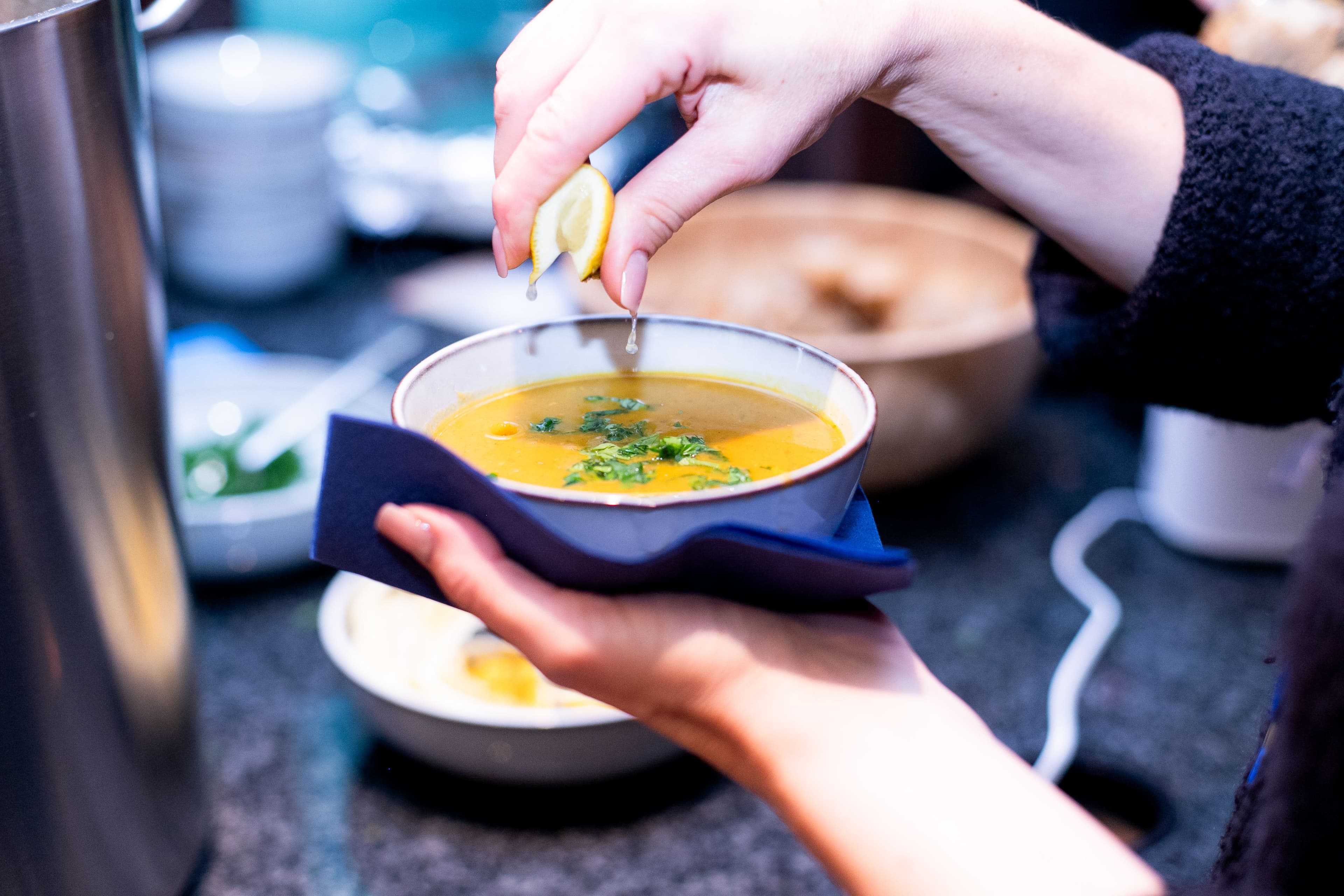 Eine Hand drückt eine Zitronenscheibe über einer Suppe aus