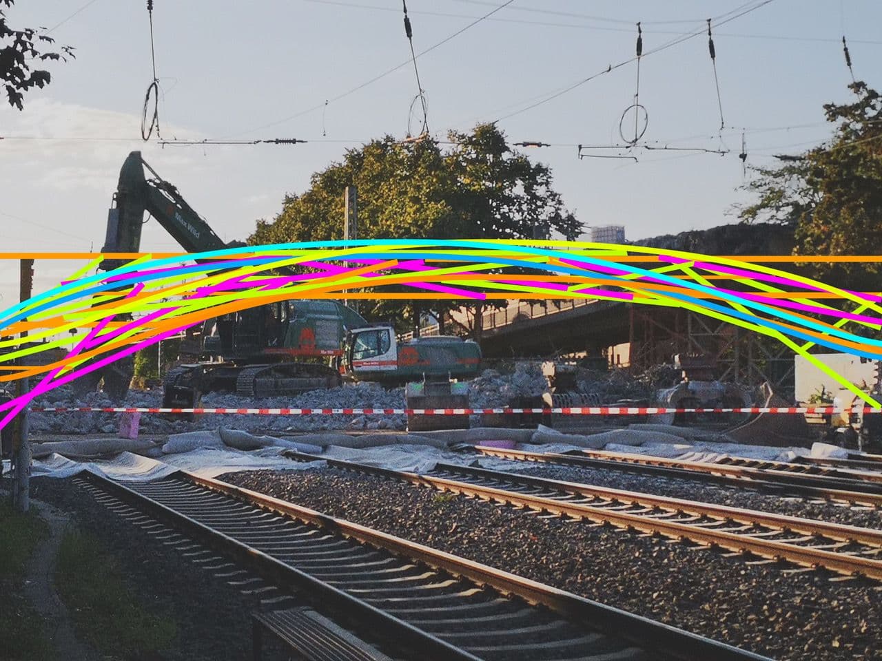 Bunte gemalte Striche liegen über einem Foto einer Baustelle an Bahngleisen