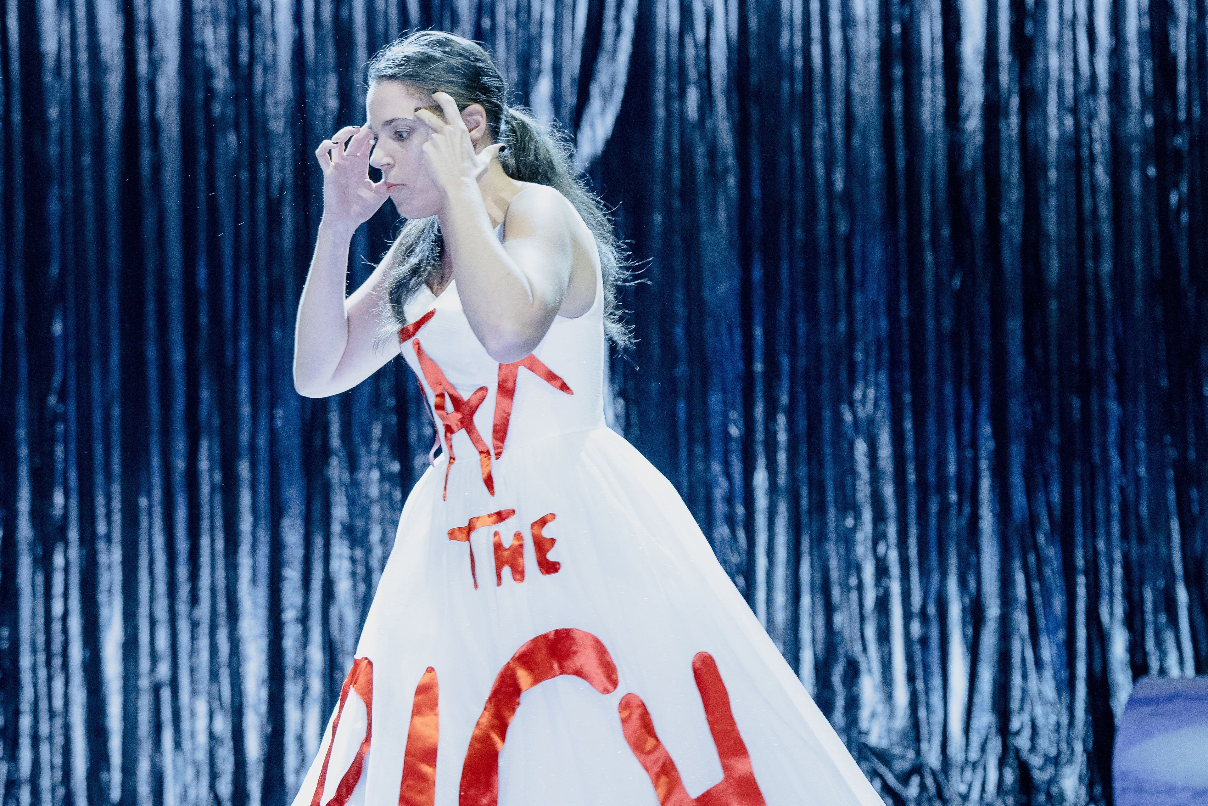 Eine Frau steht auf einer Theaterbühne und trägt ein Kleid mit der Aufschrift "Tax the rich"
