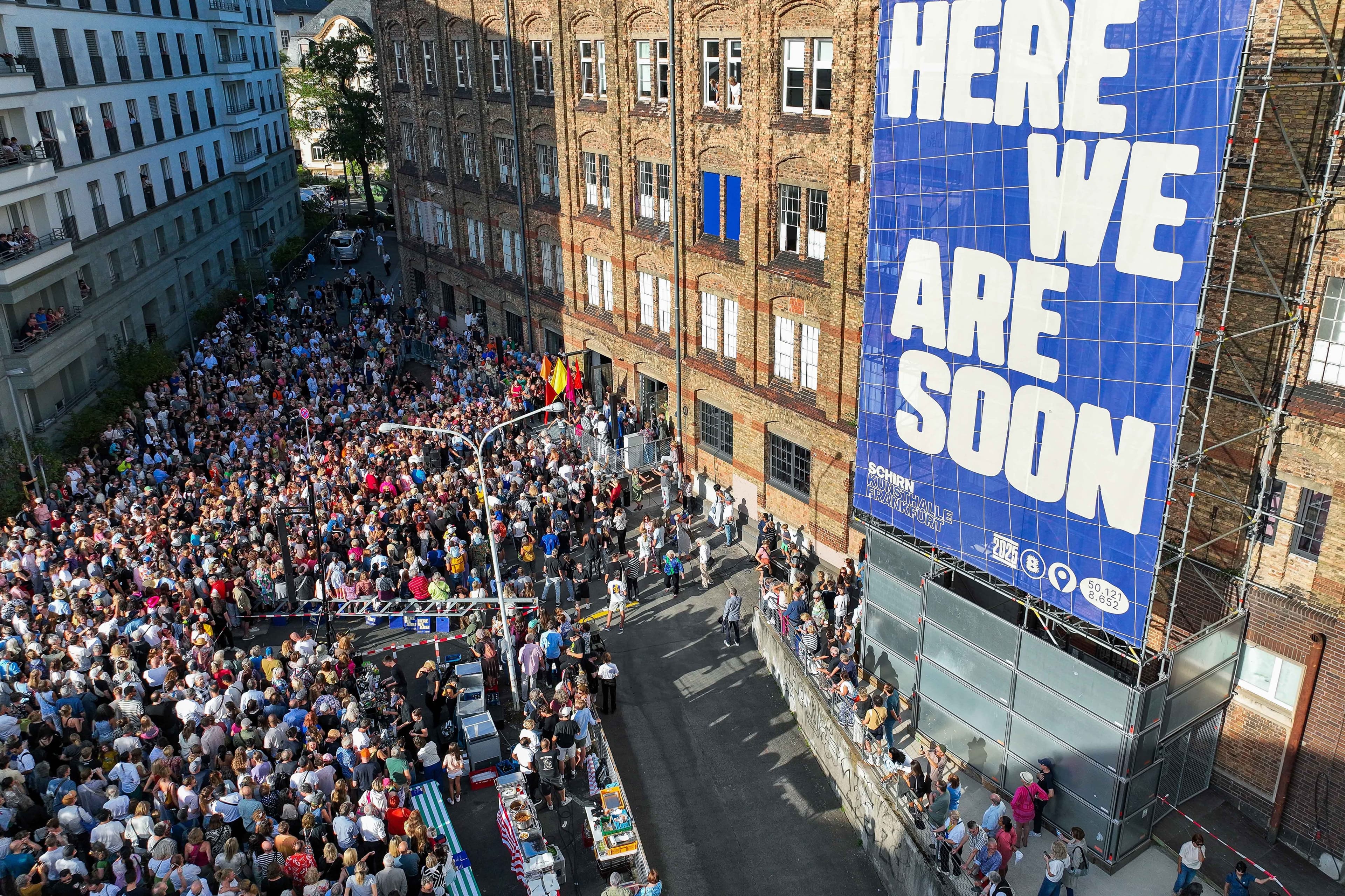 Aus der Vogelperspektive ist vor einem Backsteingebäude eine große Menschenmasse zu sehen.
