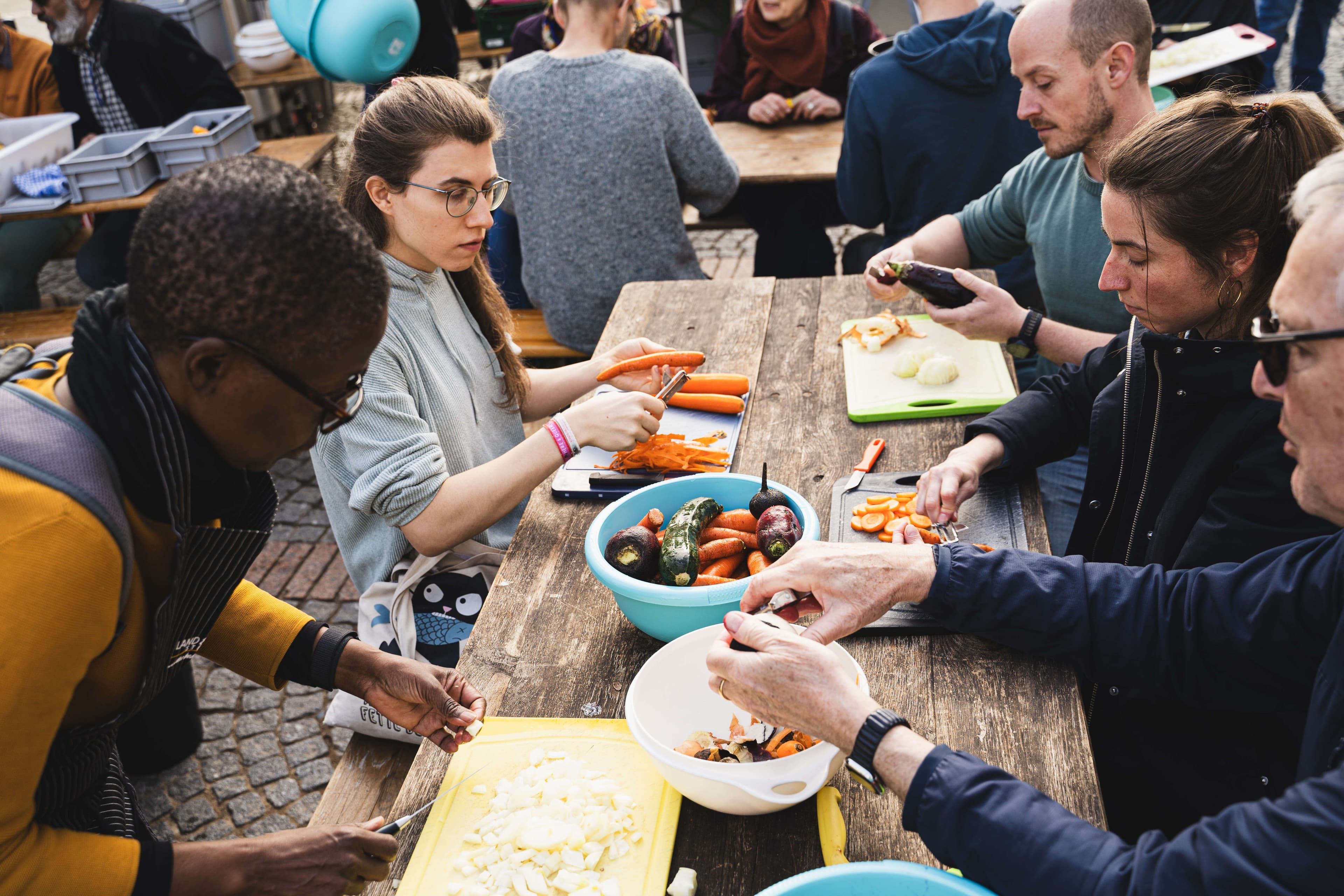 Menschen sitzten gemeinsam an einem Tisch und schneiden verschiedenes Gemüse