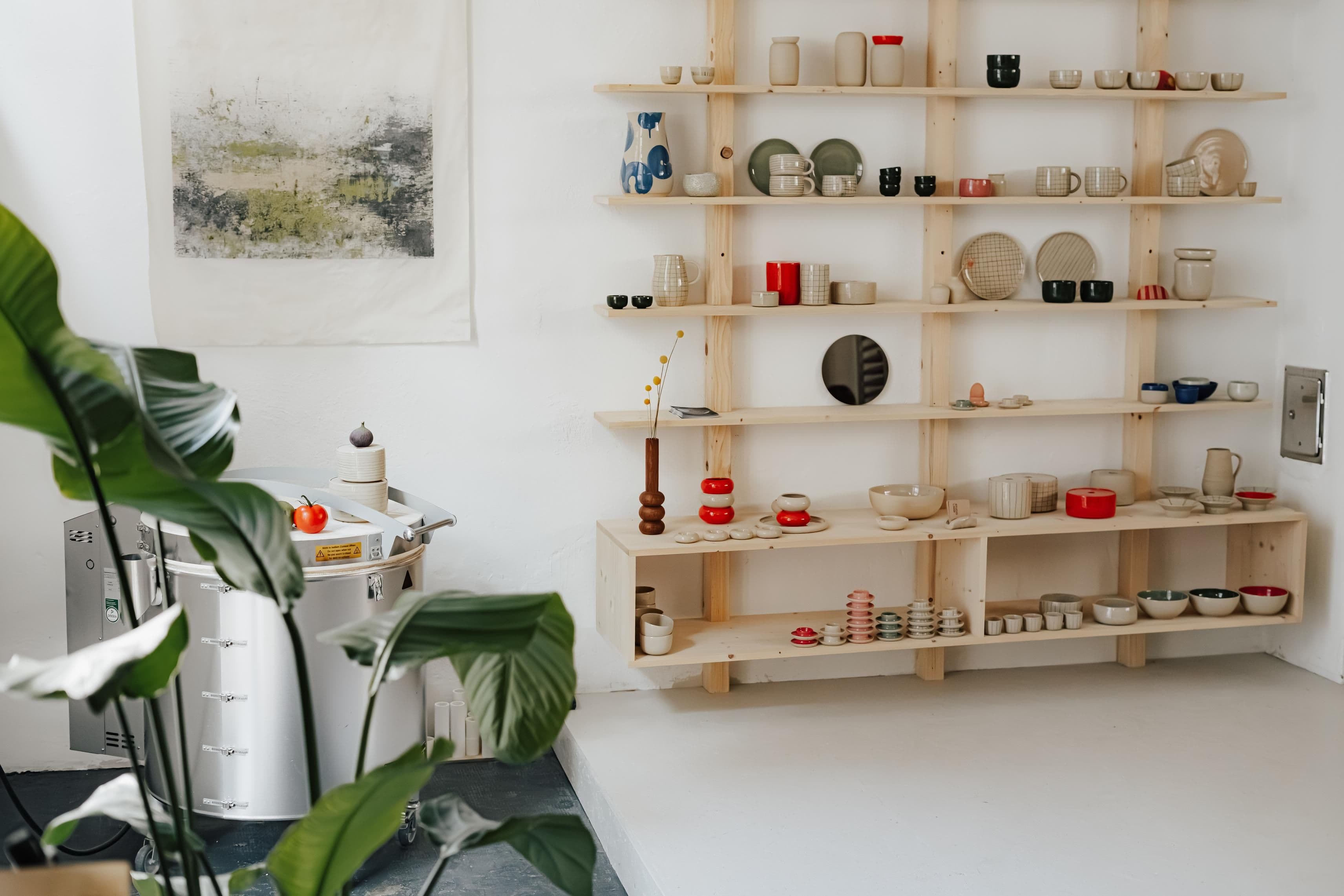 Blick in ein helles, freundliches Studio mit einem Holzregal in dem Keramik steht