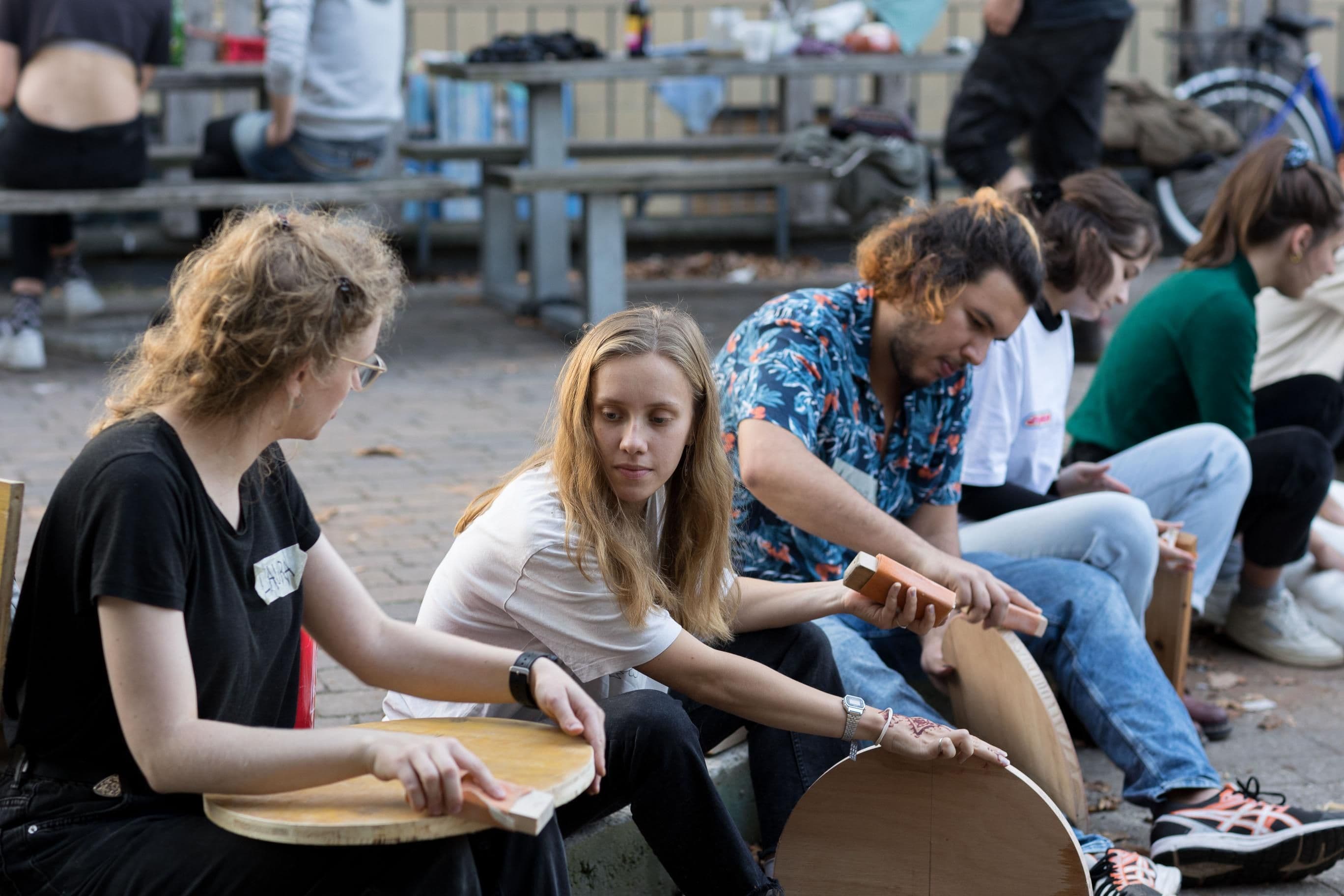 Mehrere Menschen sitzen auf dem Boden und bauen Sitzmöbel aus Holz.