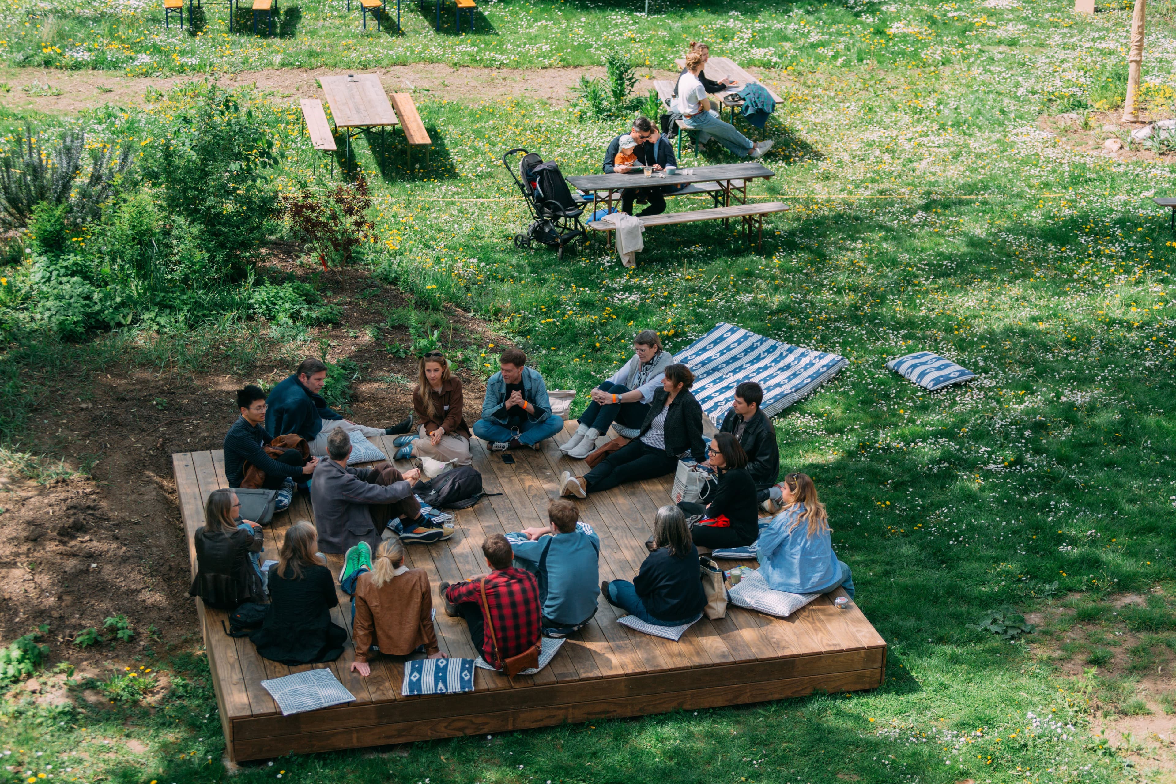 Menschen sitzen in einem Kreis auf einer Wiese bei gutem Wetter