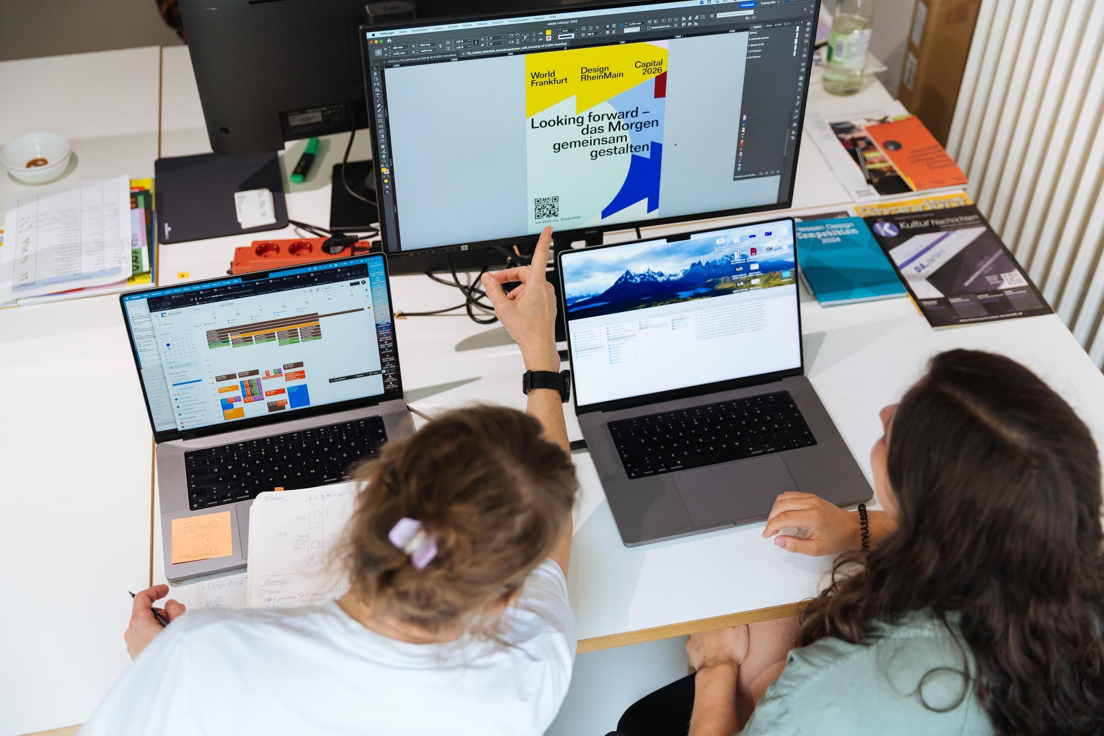 Zwei Personen sitzen an einem Tisch im Büro und diskutieren über ein Plakat.